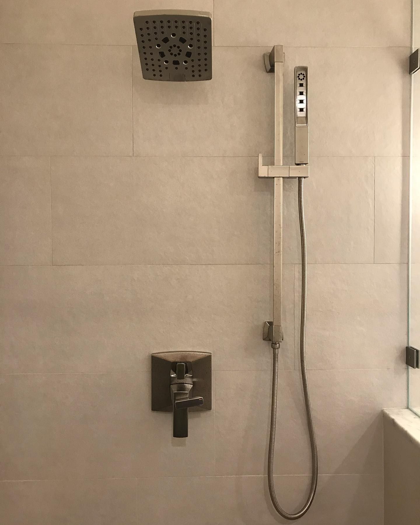 A modern brushed-nickel shower system featuring a square overhead rainfall head, a handheld sprayer on a bar, and a mixer.