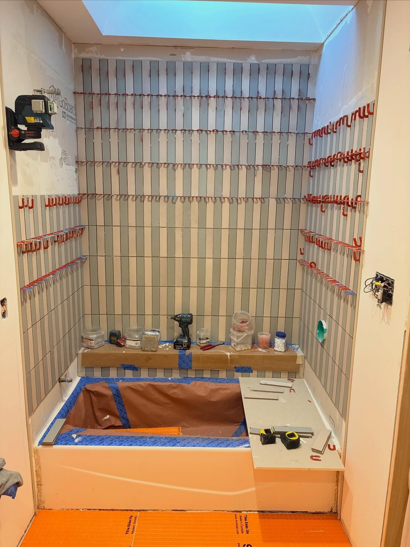 A bathroom renovation in progress, featuring tiled walls, a bathtub covered in protective paper, and an orange floor base.