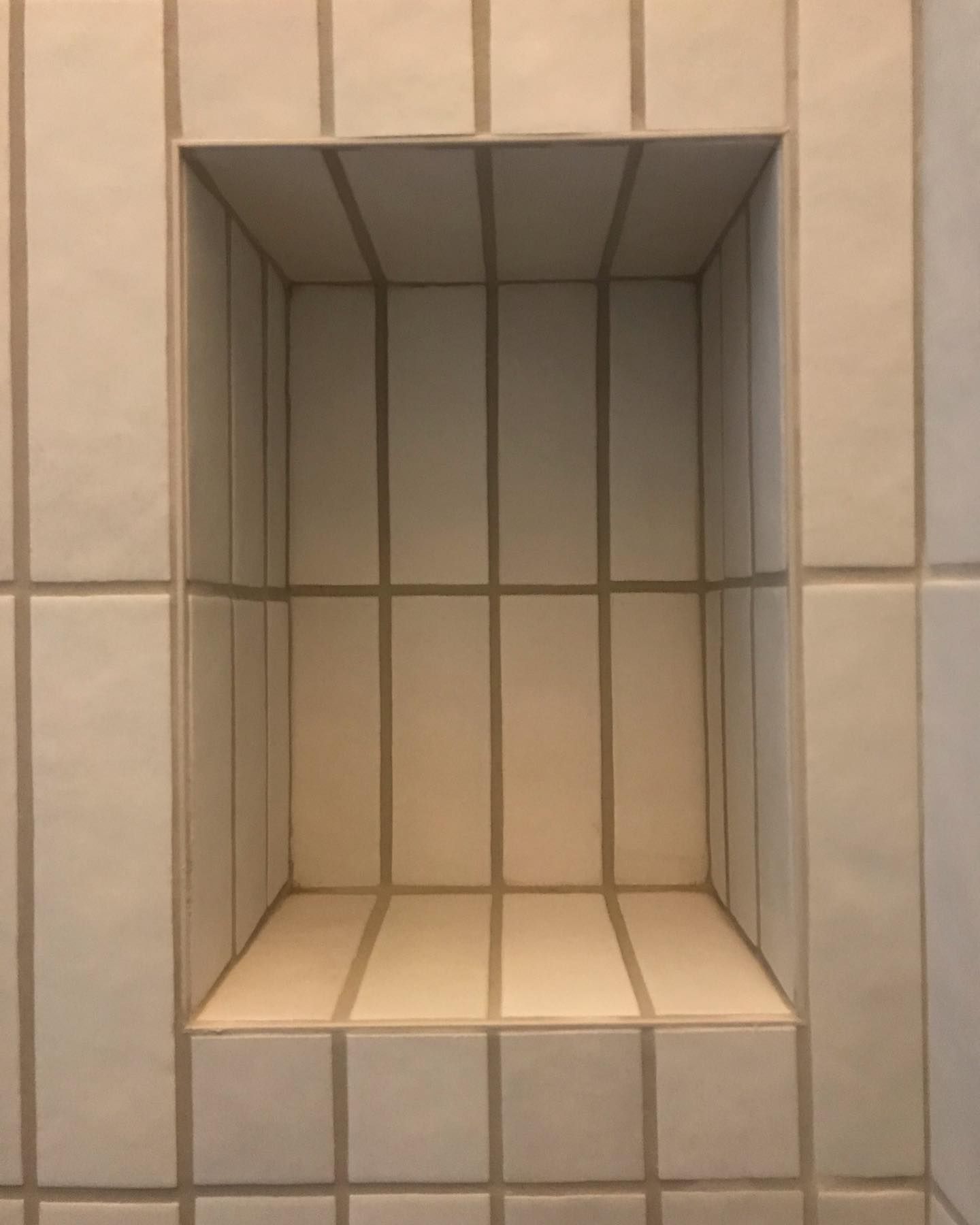 A recessed rectangular shower niche with off-white vertical subway tiles and light-colored grout on a matching tile wall.