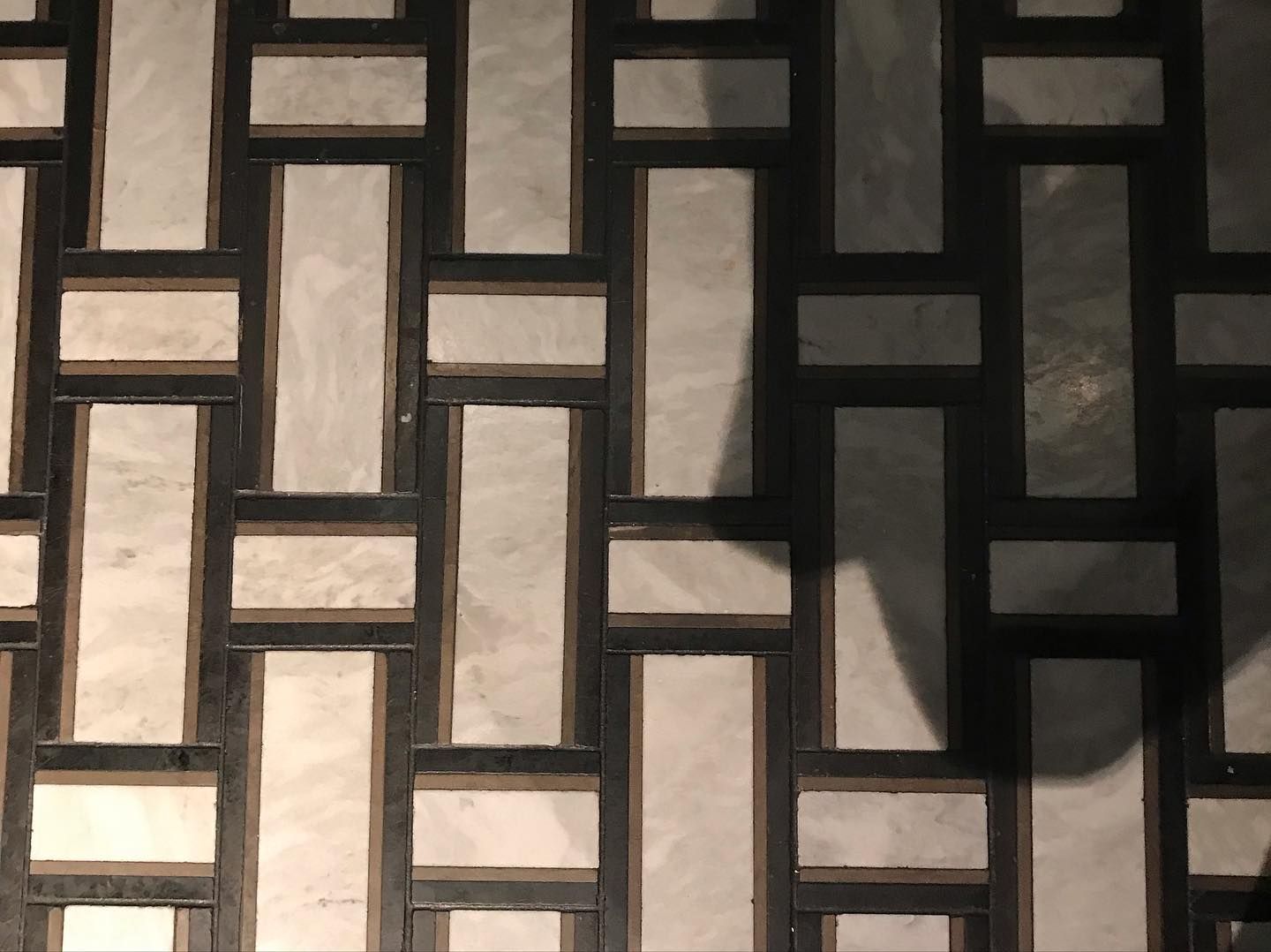 A floor pattern of vertical and horizontal light gray rectangular marble tiles separated by thin black borders.