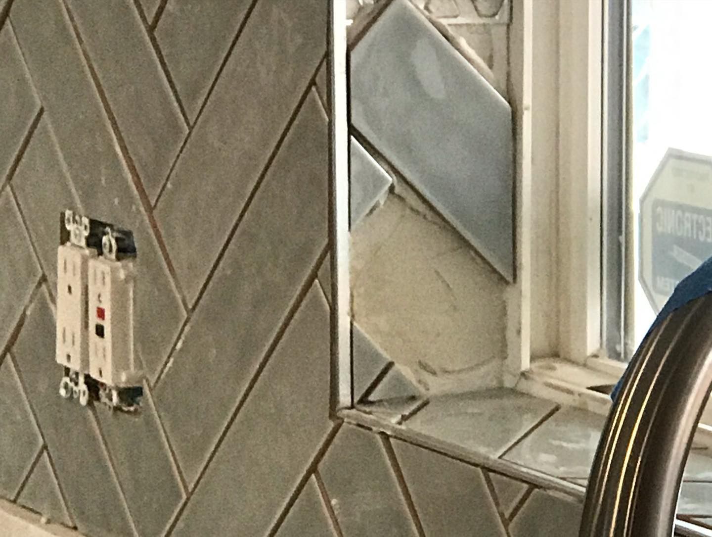 Gray herringbone backsplash tile installed around a window frame with an exposed gap and electrical outlet.