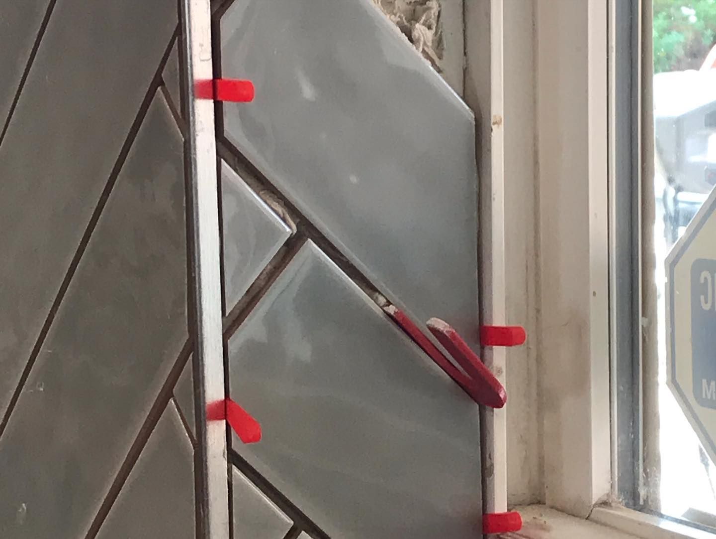Gray tiles installed in a herringbone pattern with red leveling clips against a white window frame.