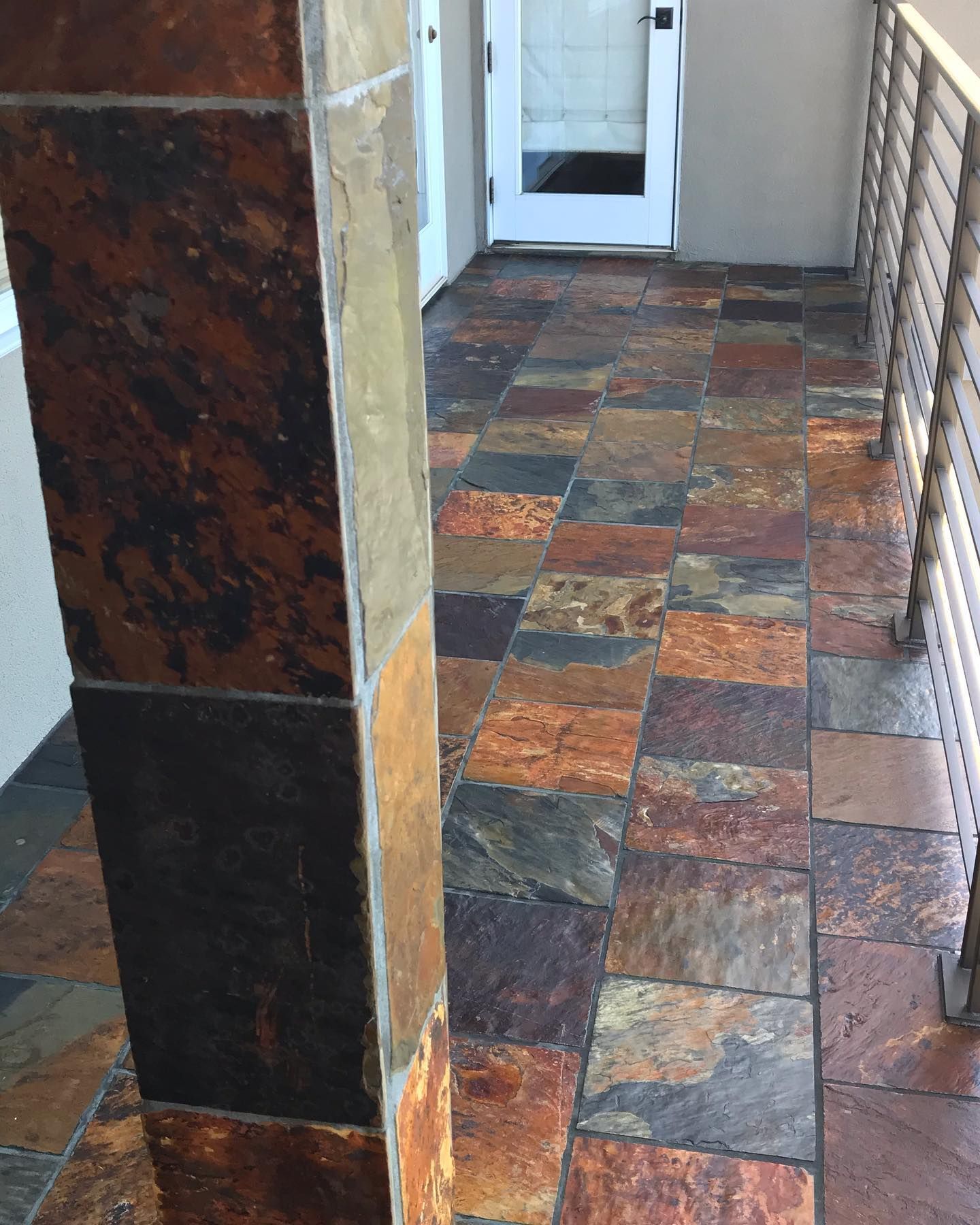 A porch with a square stone pillar and floor tiles in earthy shades of brown, rust, gray, and tan.
