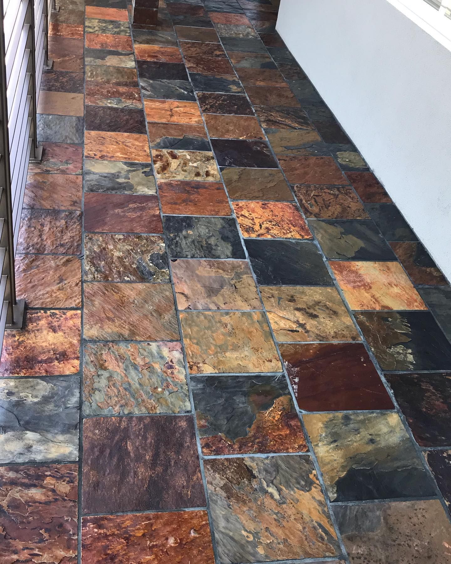 A close-up view of a patio floor covered in square, multi-colored slate tiles with earthy tones of brown, red, and gray.