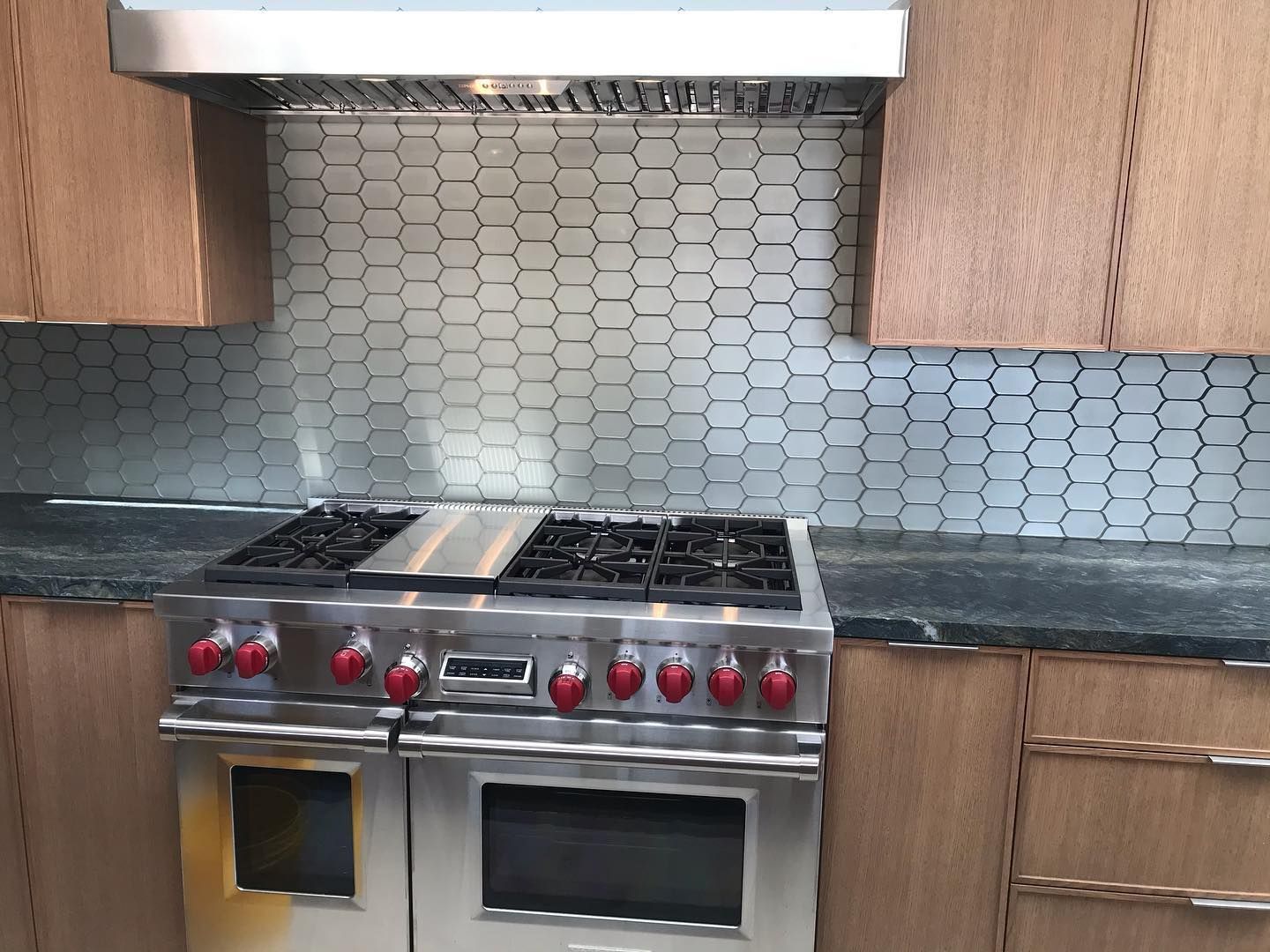 A stainless steel gas stove with red knobs sits beneath a matching range hood