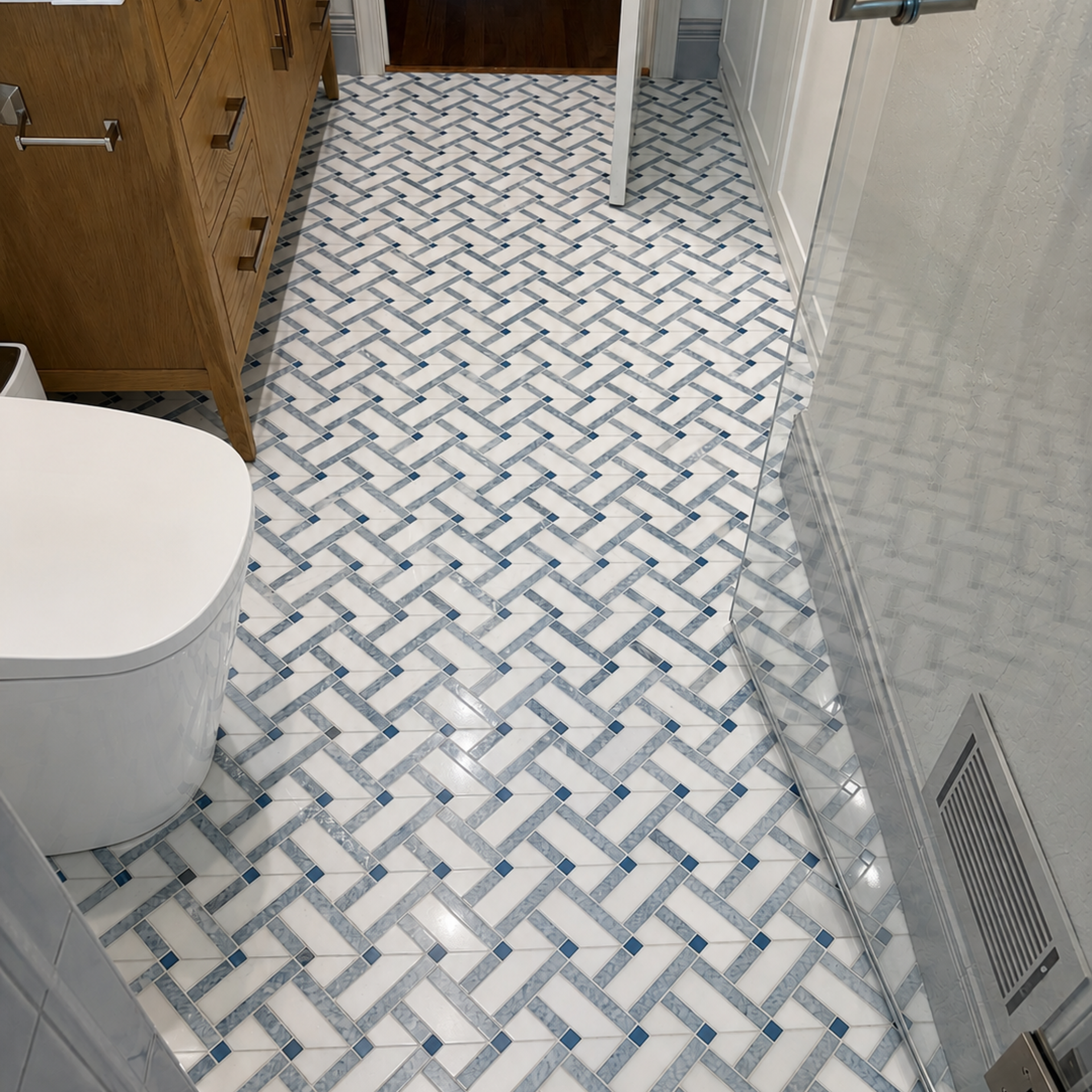 Bathroom floor with white-and-blue herringbone tile, toilet at left, and cabinet and vent along the walls