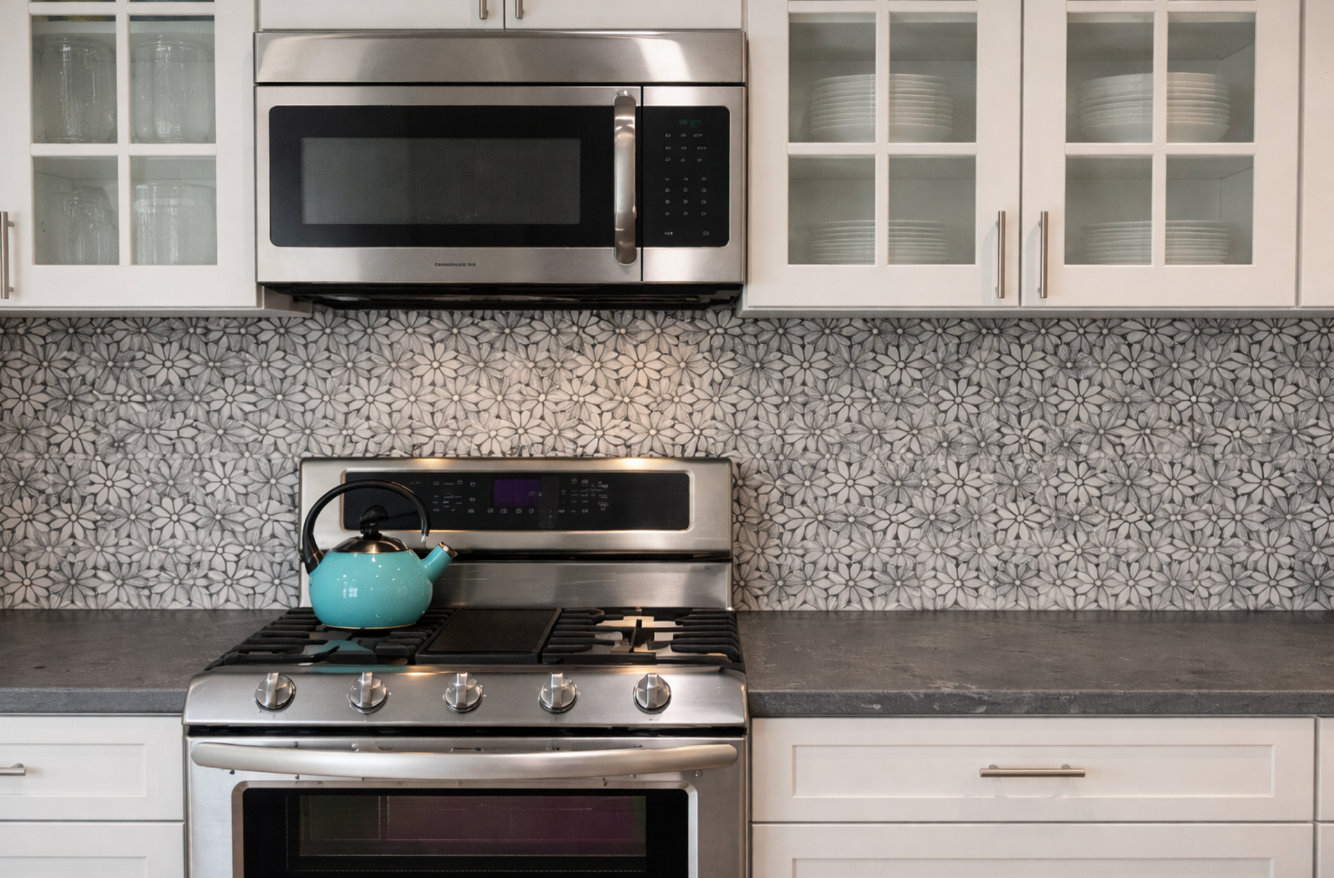Modern kitchen with teal hexagon tile backsplash, white cabinets, and stainless steel stove.