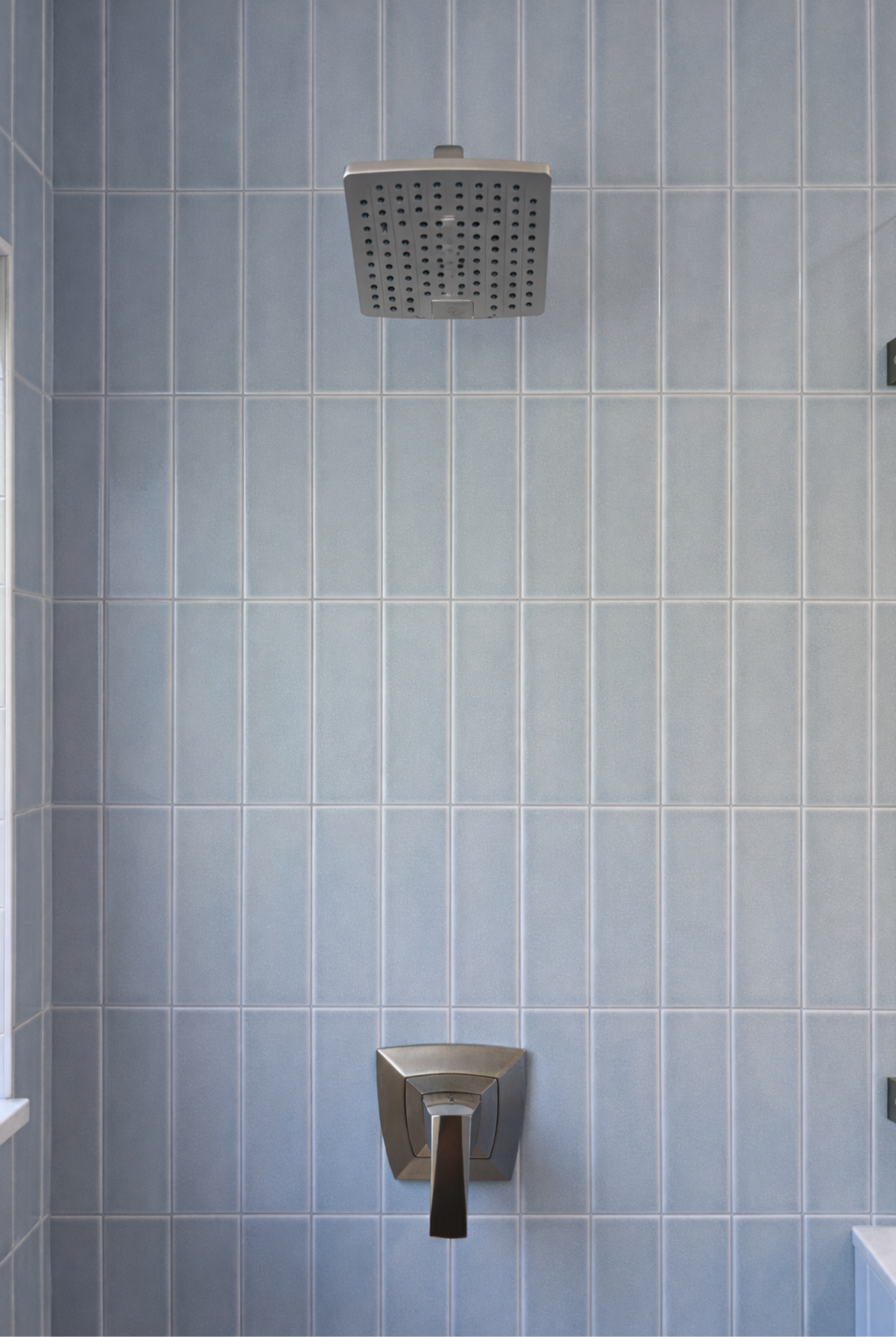 A tiled shower wall with a square rain showerhead and a lower faucet control.