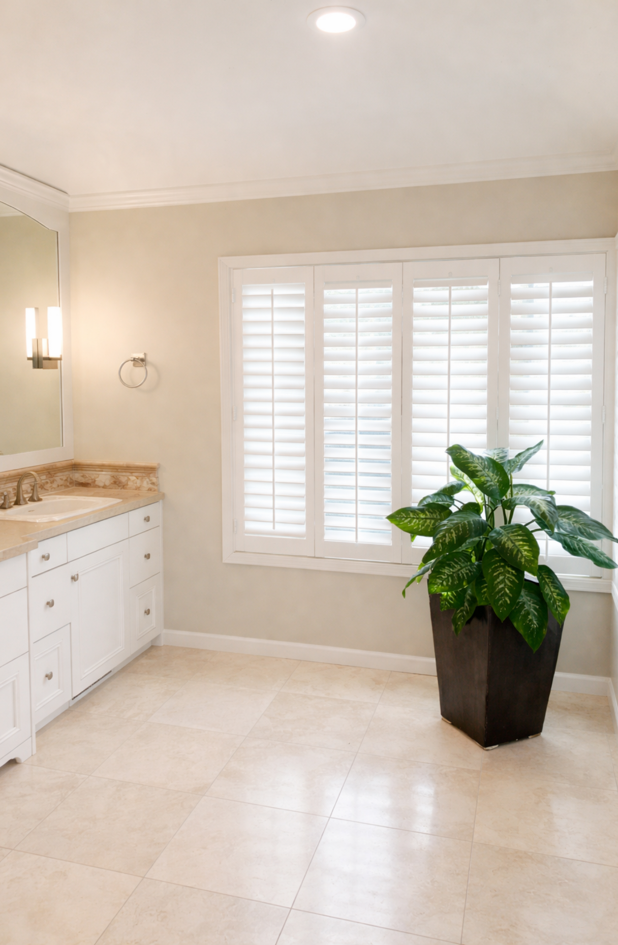 Bright bathroom with white shutters, beige walls, marble vanity, and a potted plant on the floor.