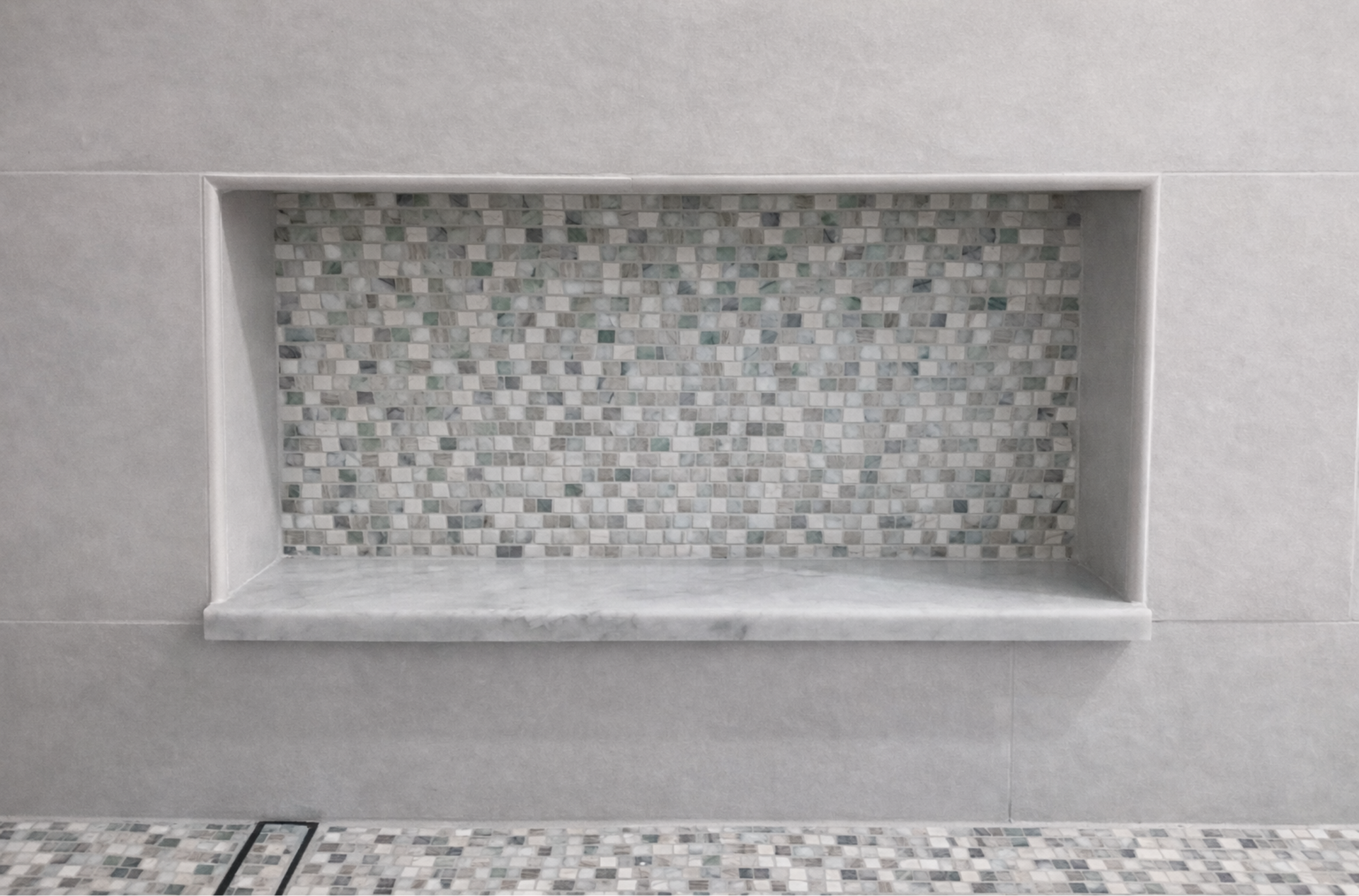 Empty recessed wall niche with gray mosaic tile backing and ledge behind a tiled surface