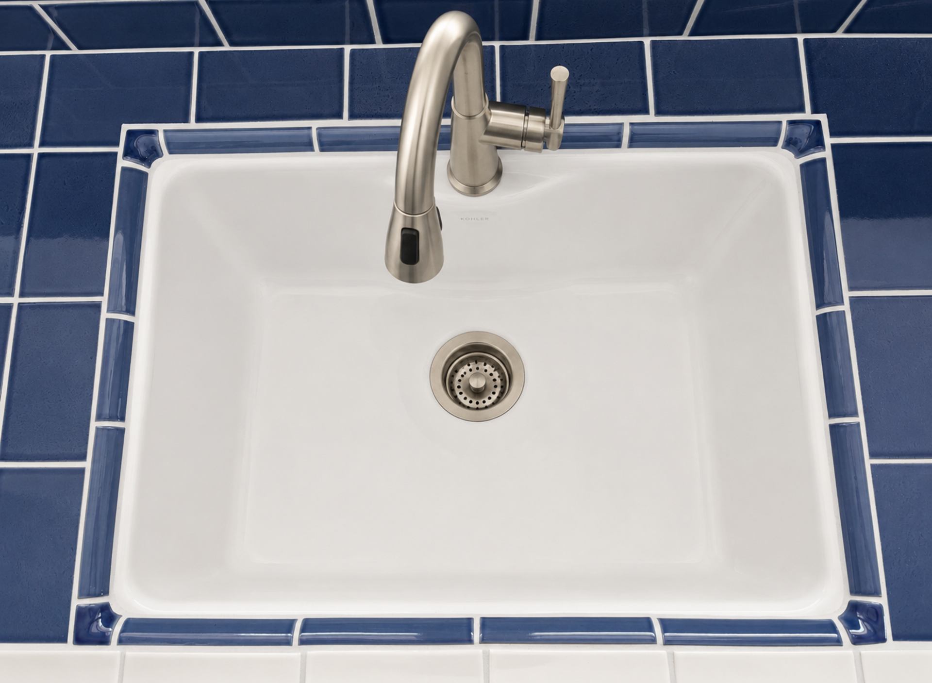 White sink with chrome faucet, set in a blue-tiled countertop.