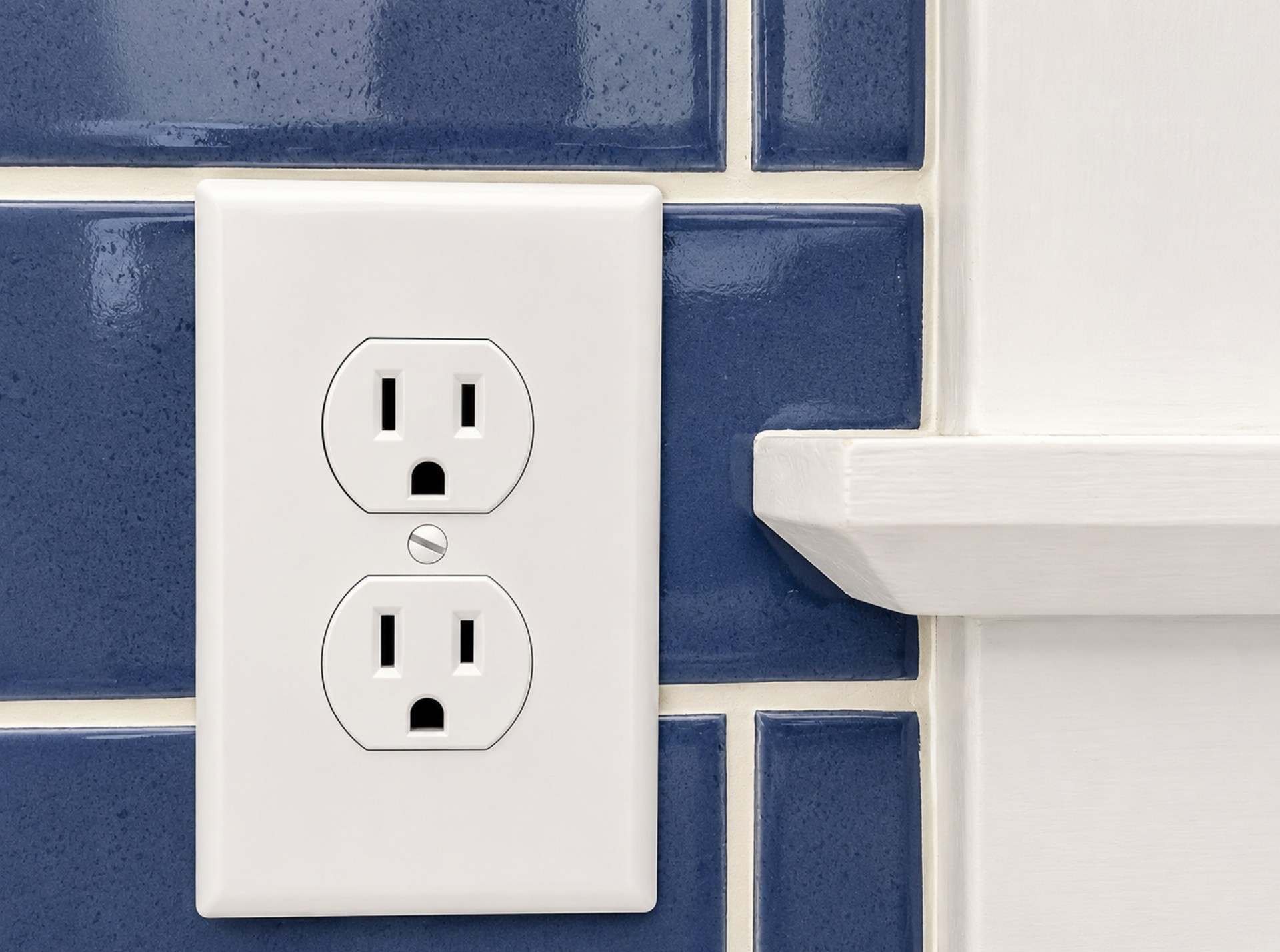 White duplex electrical outlet on blue tile wall beside a white shelf.