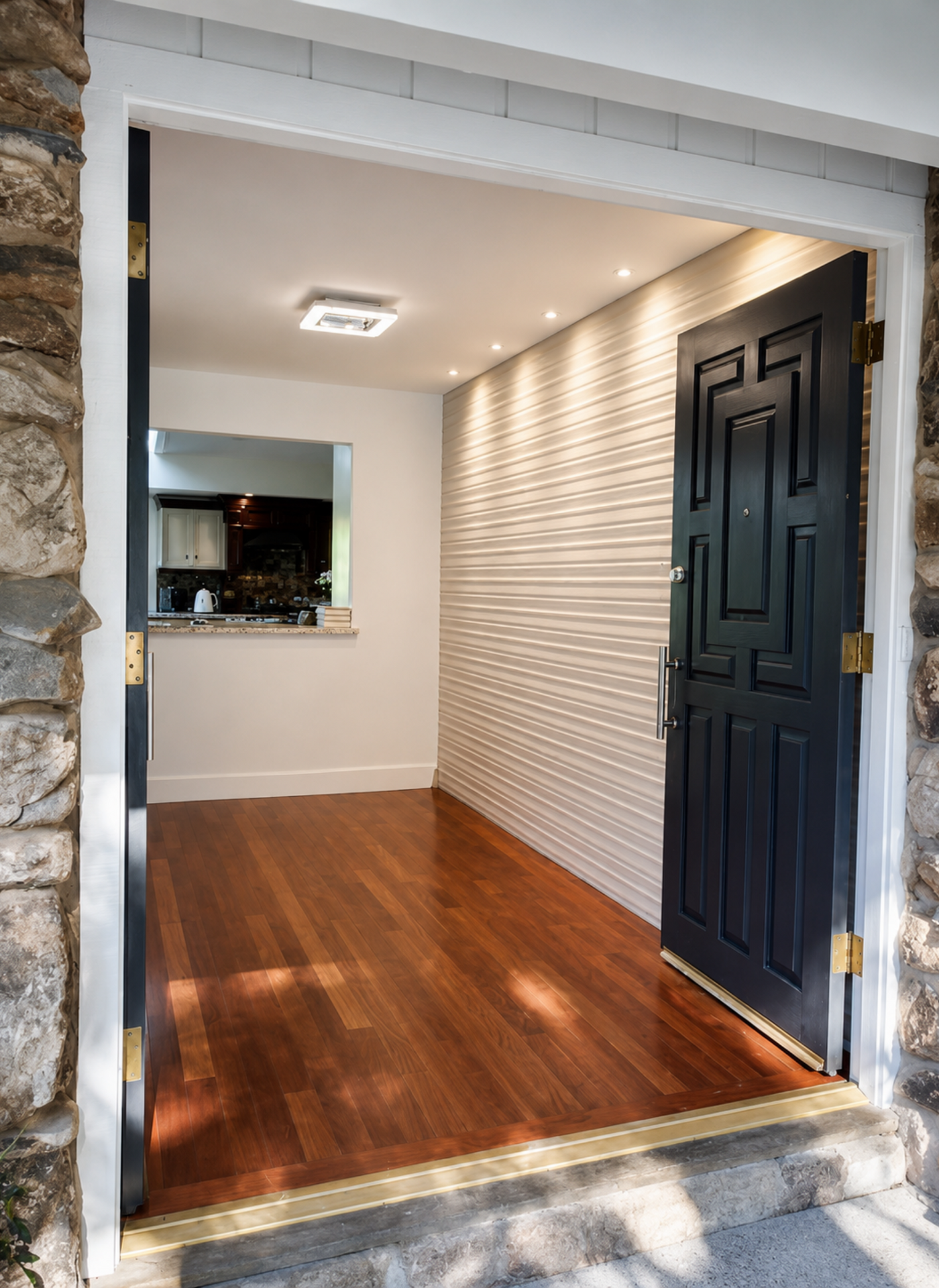 Empty entryway with wood floor, white textured walls, and an open black door under recessed lighting