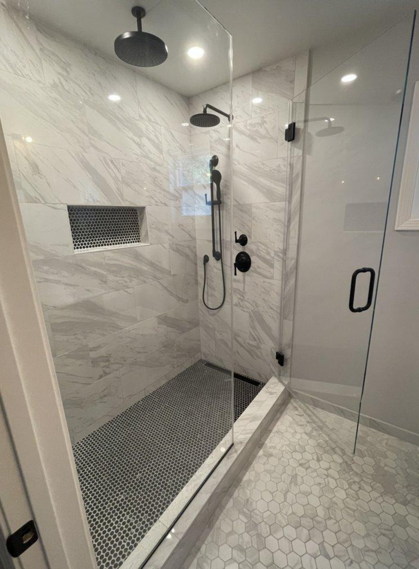 Modern glass shower with marble tile walls, black fixtures, and a pebble-tile bathroom floor