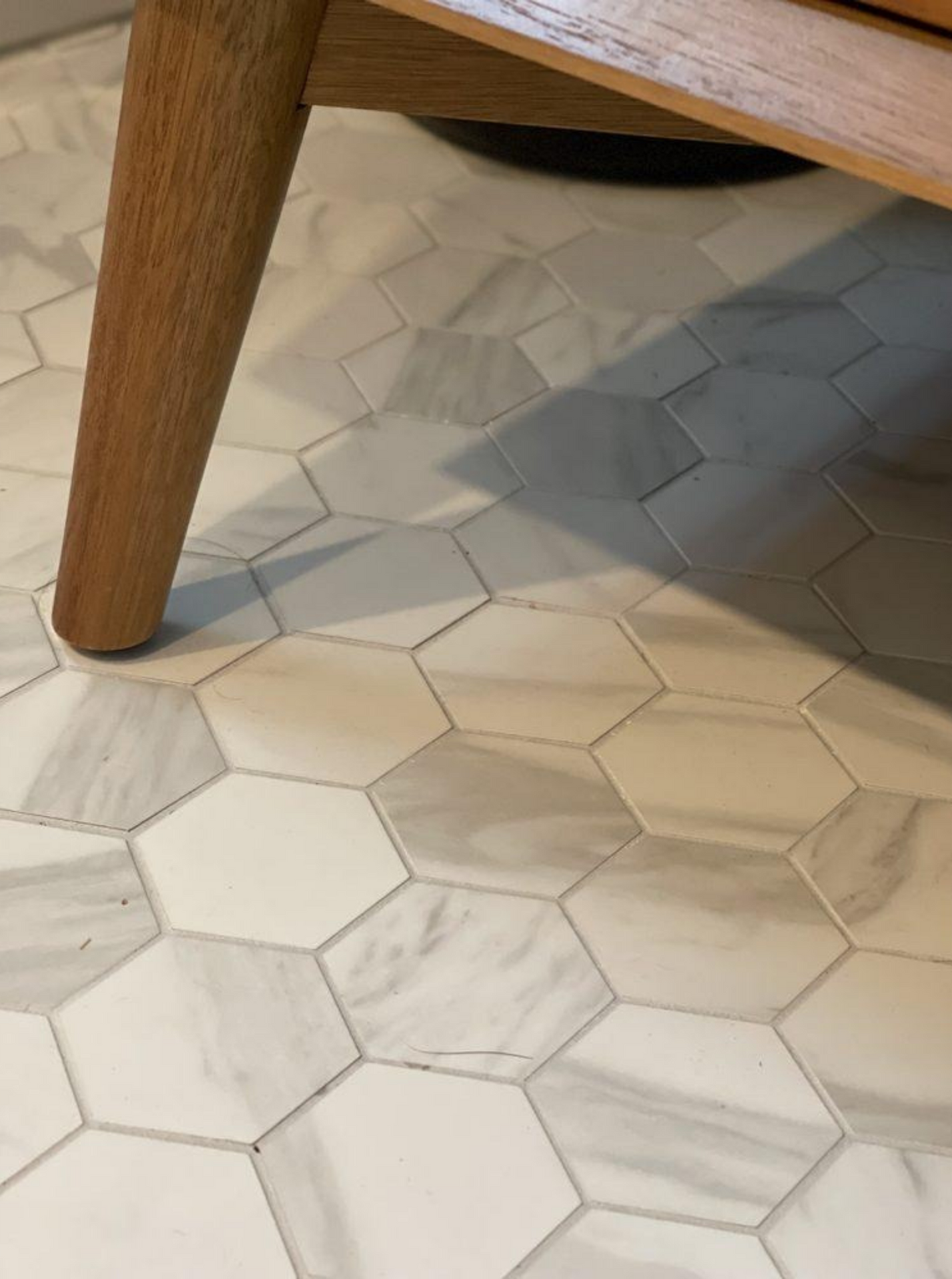 Wooden table leg on white hexagonal tile floor with subtle gray veining
