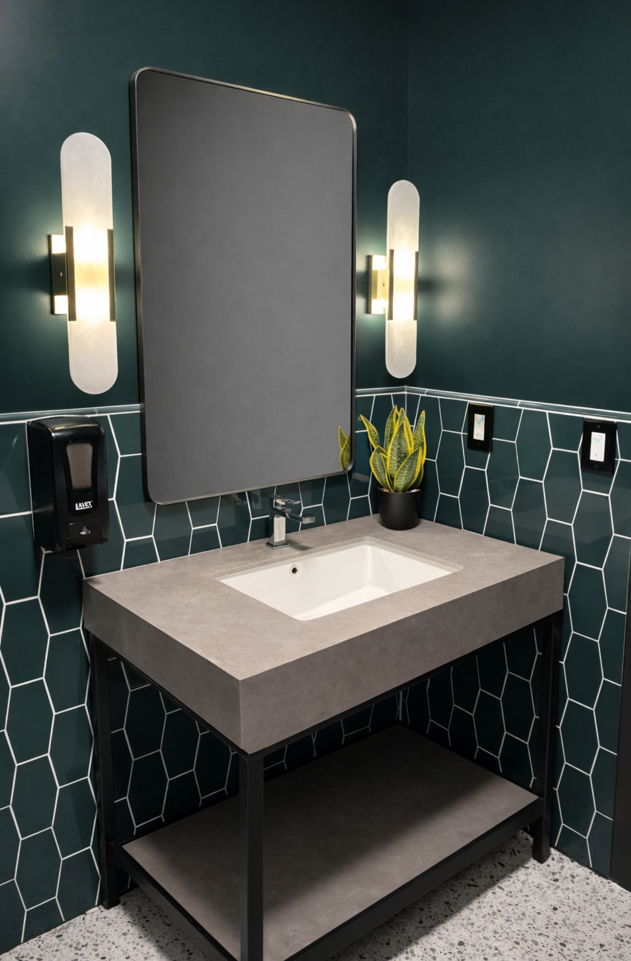 Modern bathroom vanity with gray sink, large mirror, wall sconces, and dark green tiled walls