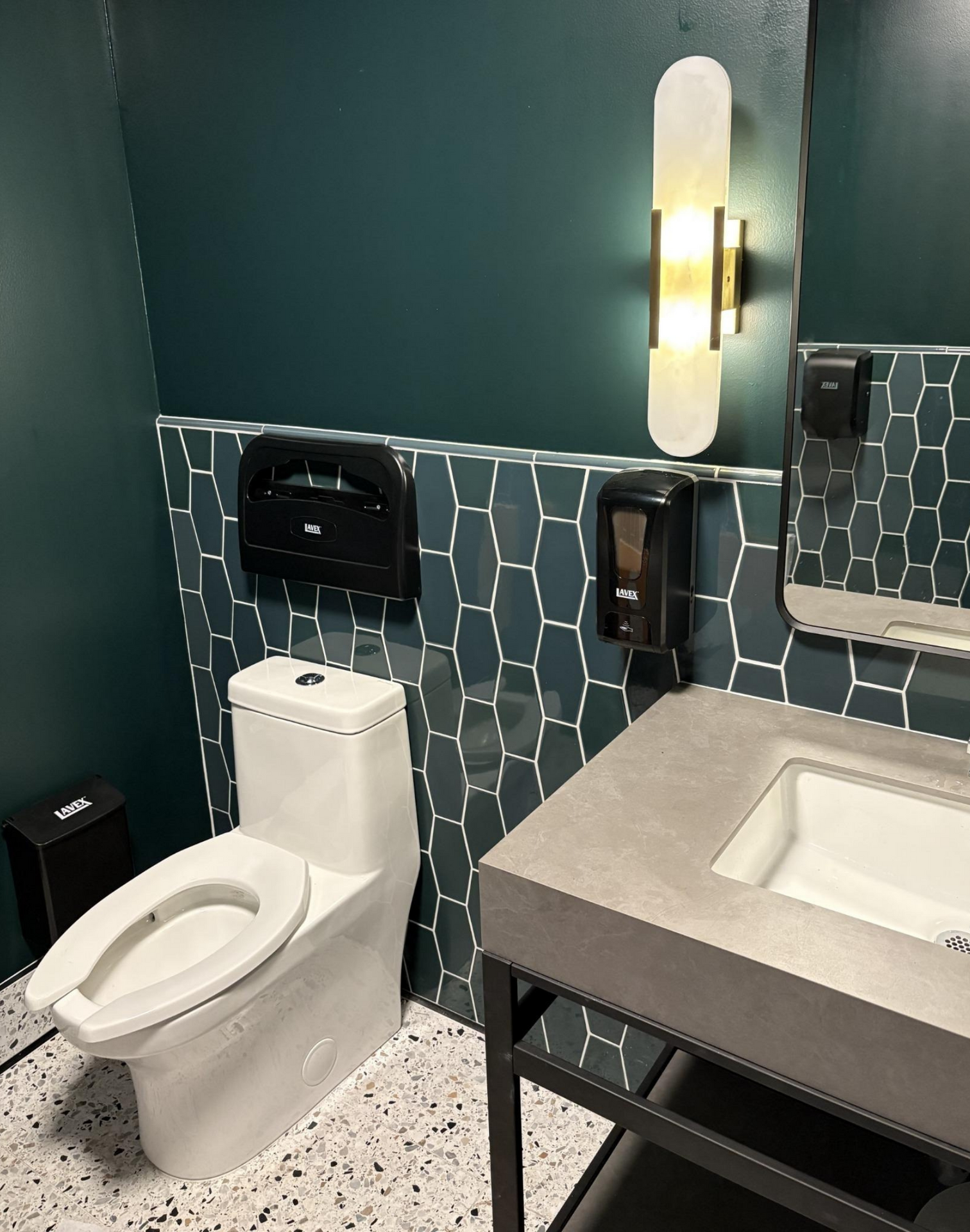 Modern restroom with toilet, sink, mirror, and teal tile accents on dark walls