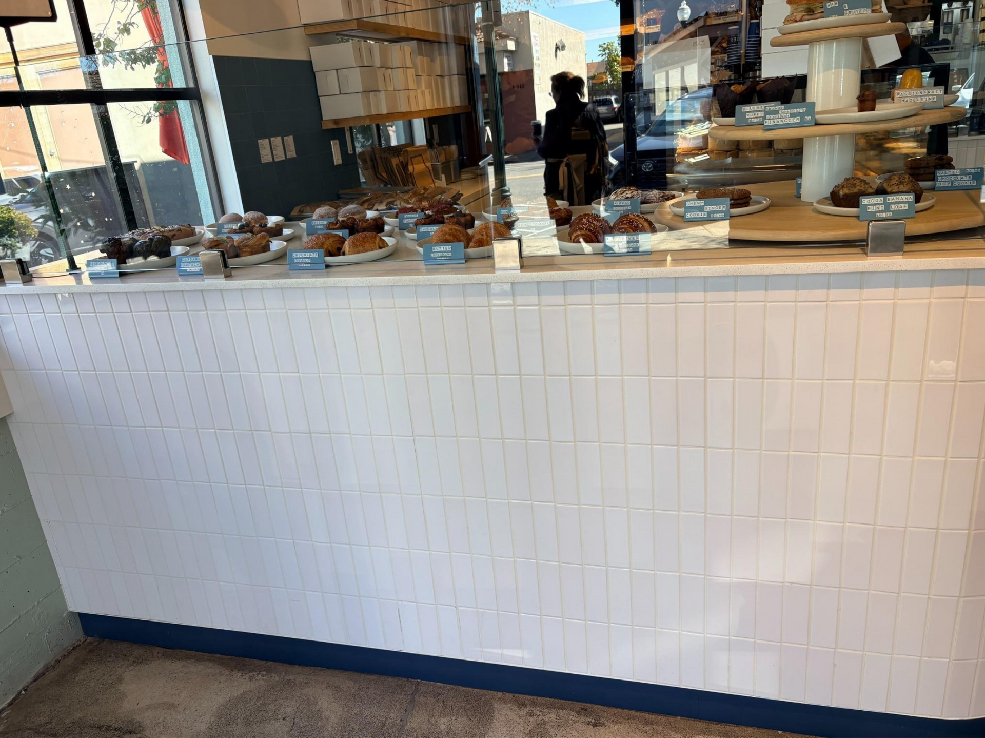 Bakery counter with pastries and cakes displayed behind a white tiled front