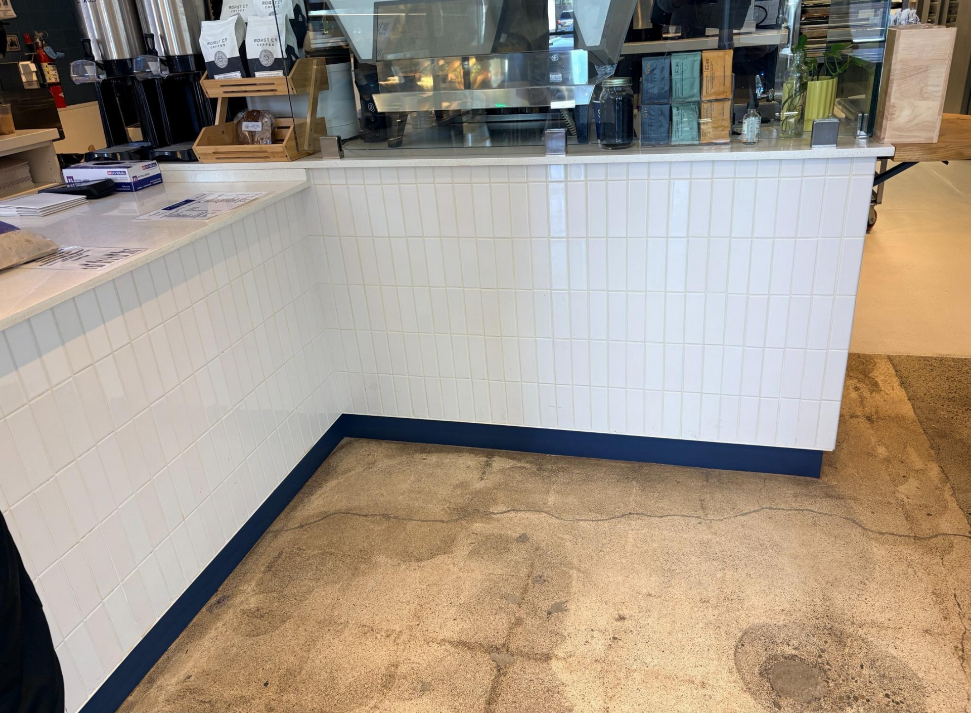 White tiled café counter with blue base trim and beige floor in front of a beverage station