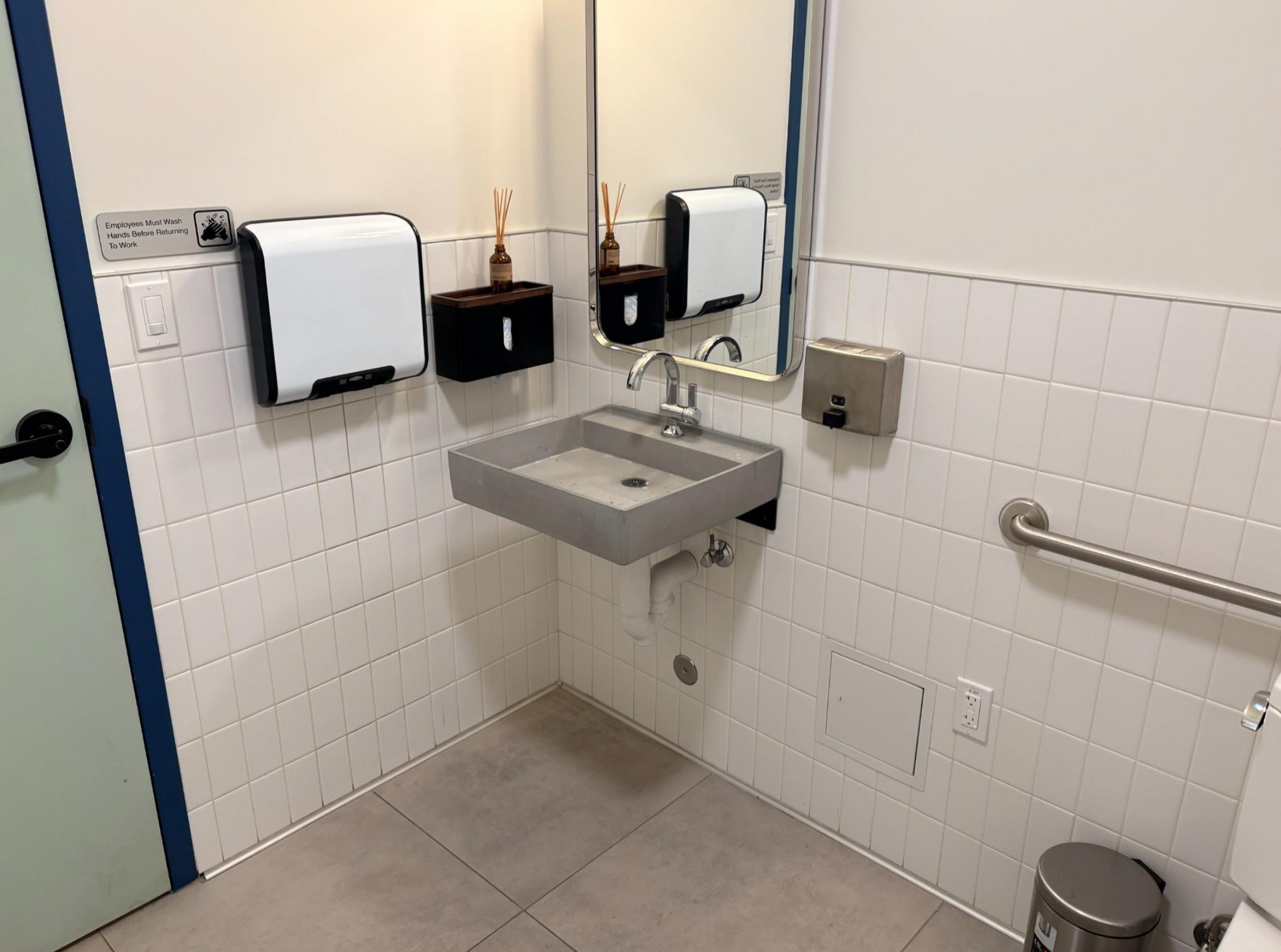 Accessible restroom with wall-mounted sink, grab bar, mirrors, and tiled walls