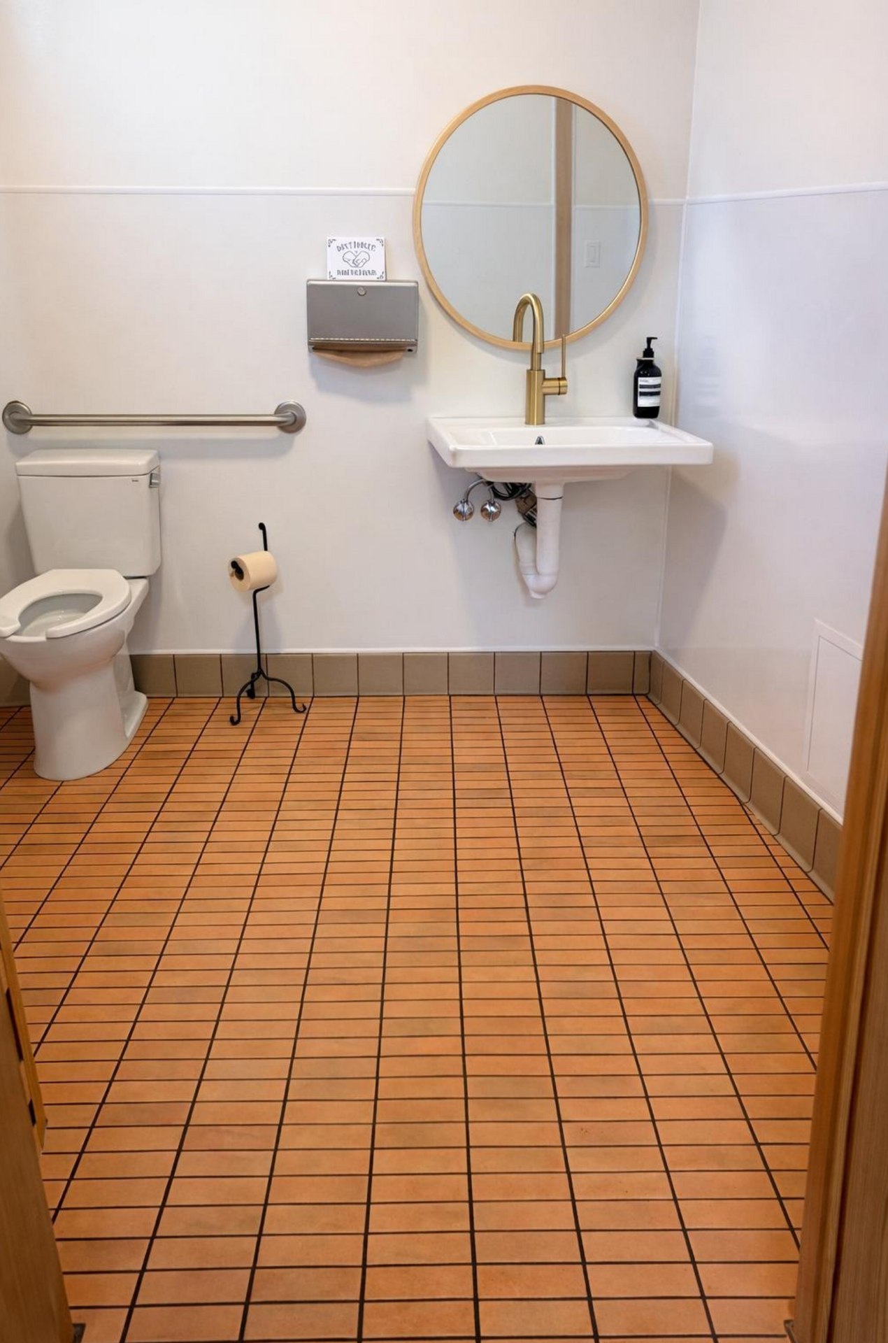 Accessible bathroom with toilet, wall sink, grab bars, and tan tiled floor