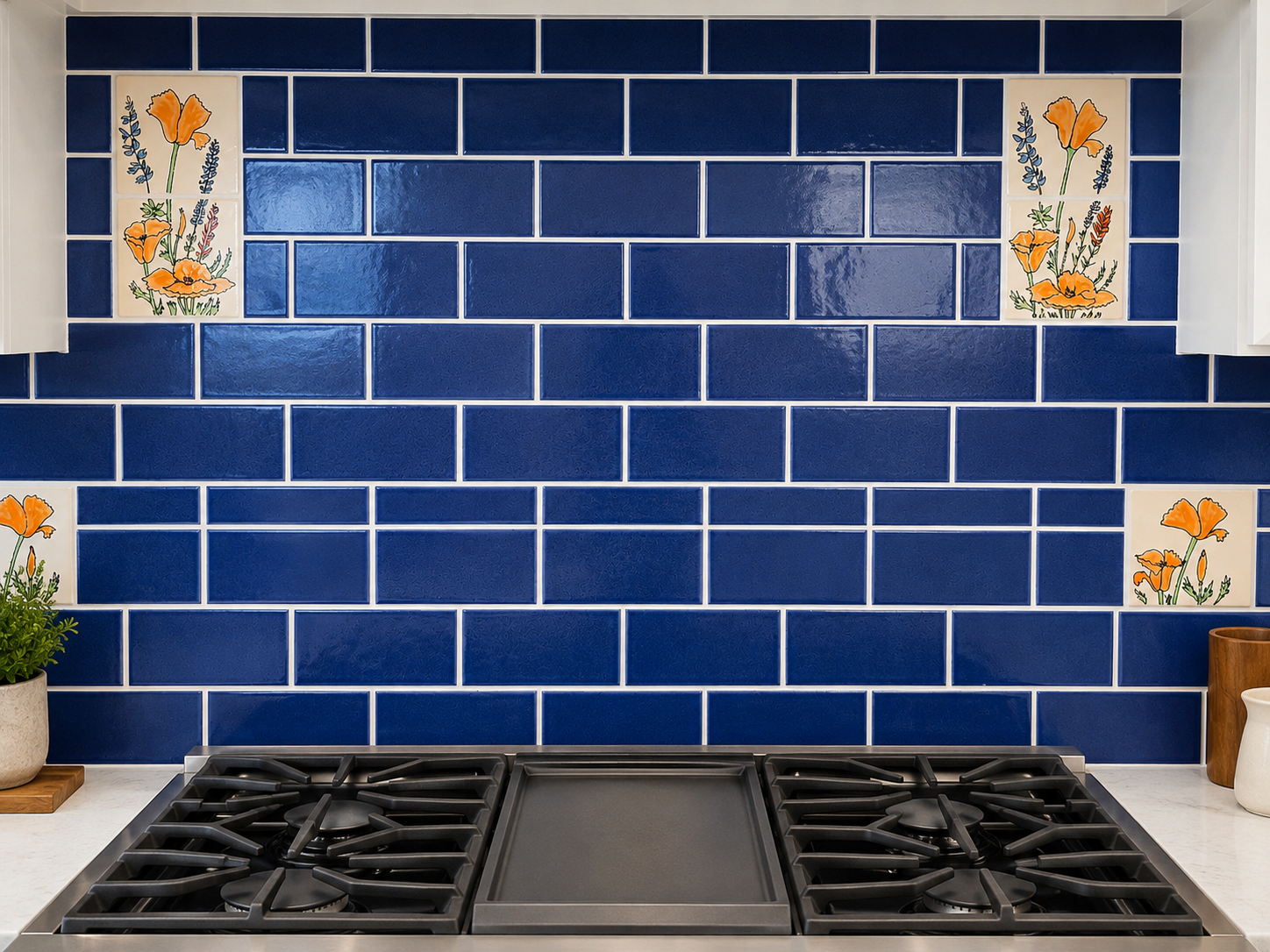Blue tiled kitchen backsplash behind a gas cooktop, with small floral accent tiles and potted plants on the counter
