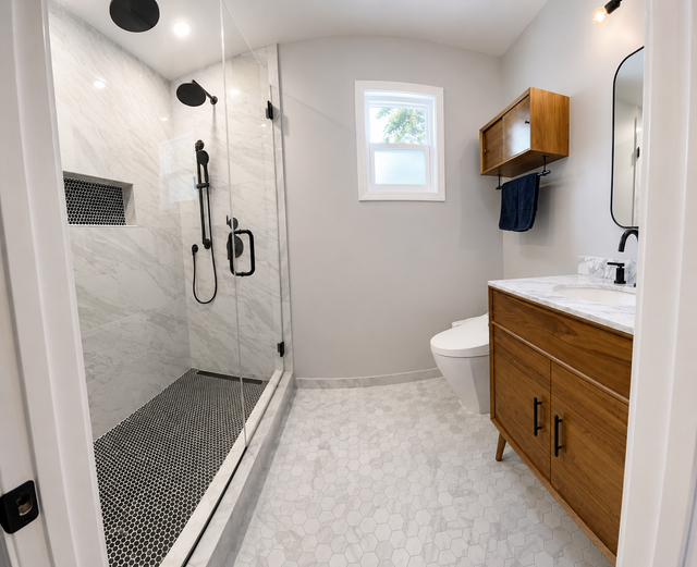 Modern bathroom with glass shower, white tile, and wood vanity with sink and mirror cabinet.