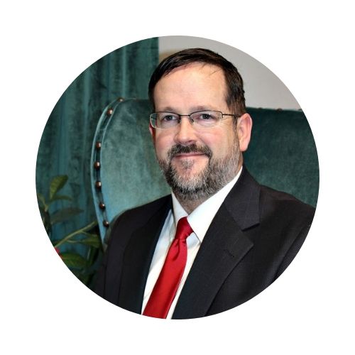 Portrait of a man in a black suit with a red tie, standing before a teal abstract background