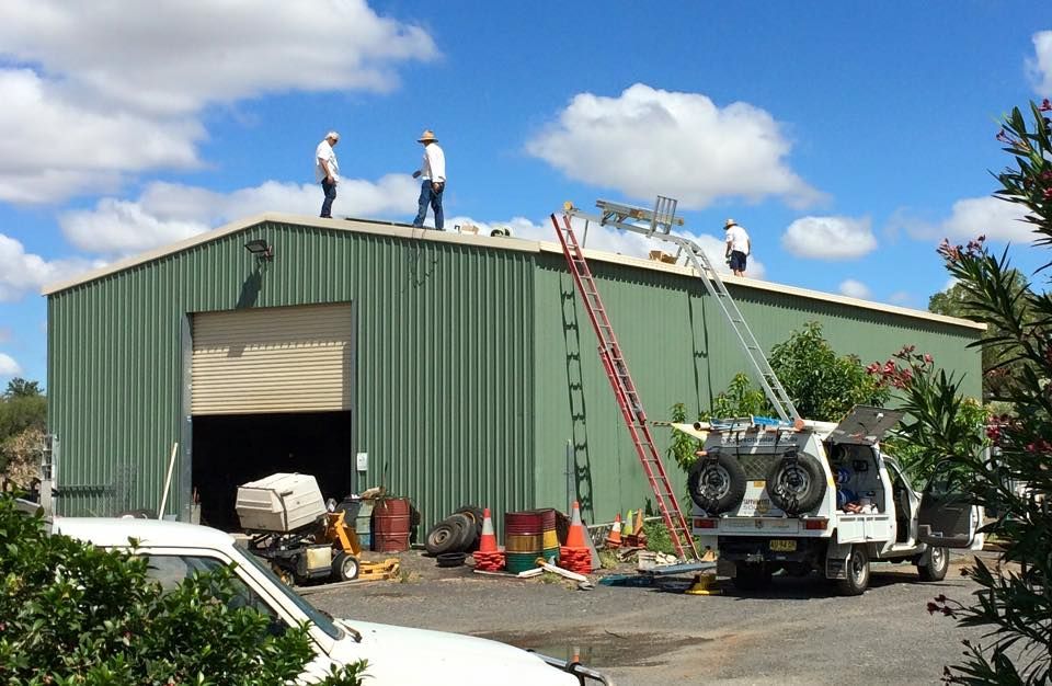 Three Men Are Working on the Roof of a Green Building — Sapphire City Solar & Electrical In Inverell, NSW