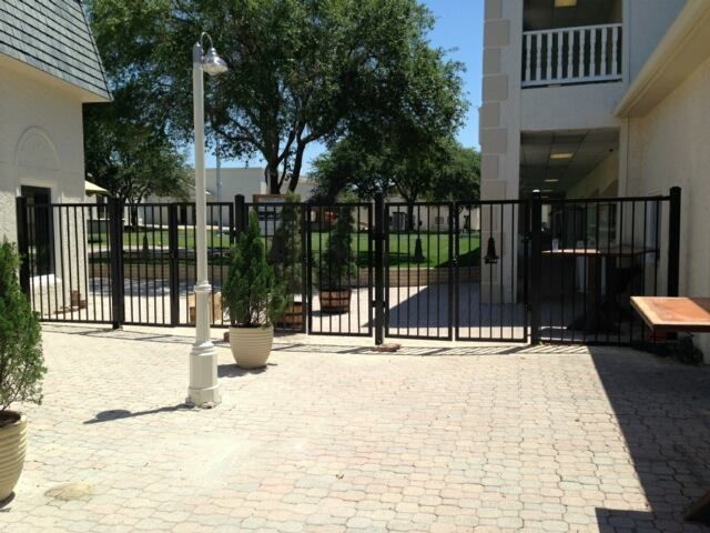 Courtyard with black metal gate, potted plants, and apartment buildings in bright sunlight