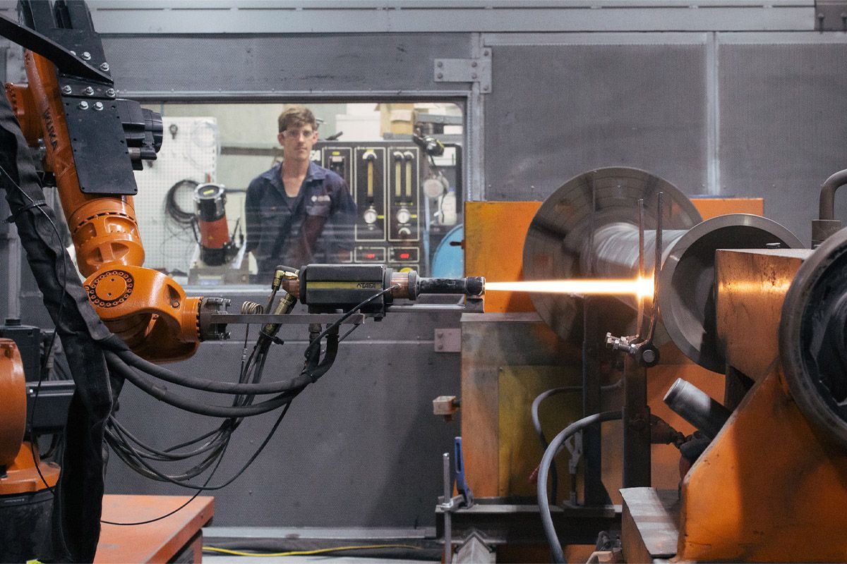 A man is standing in front of a machine at New Metal Surfaces factory.