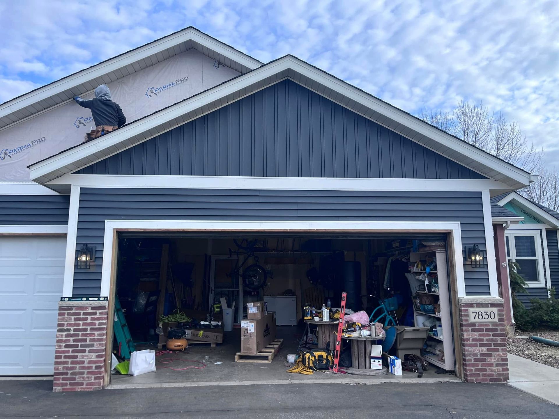 Open garage with boxes, tools, and household items under a blue gabled roof.