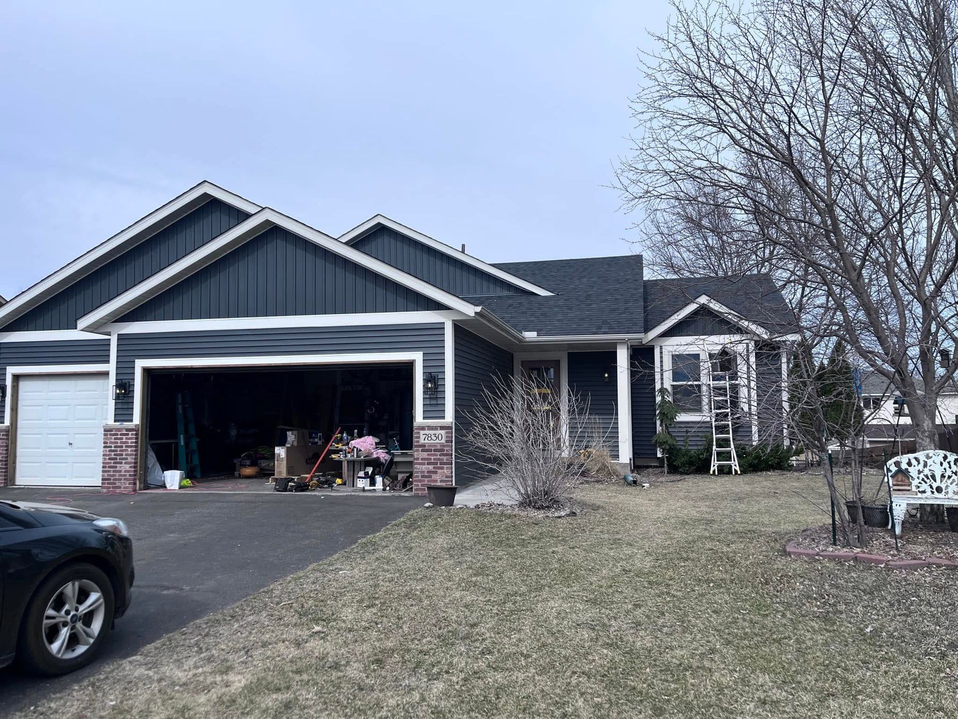 Blue-gray suburban house with open garage, driveway, and winter yard under bare trees