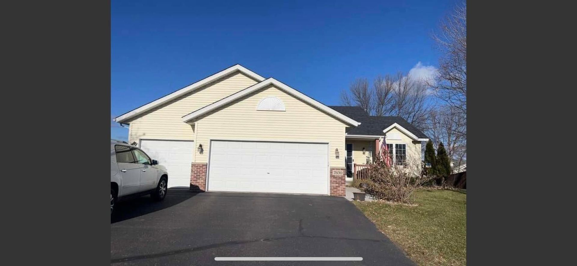 Suburban house with two-car garage, driveway, and a parked car on a sunny day