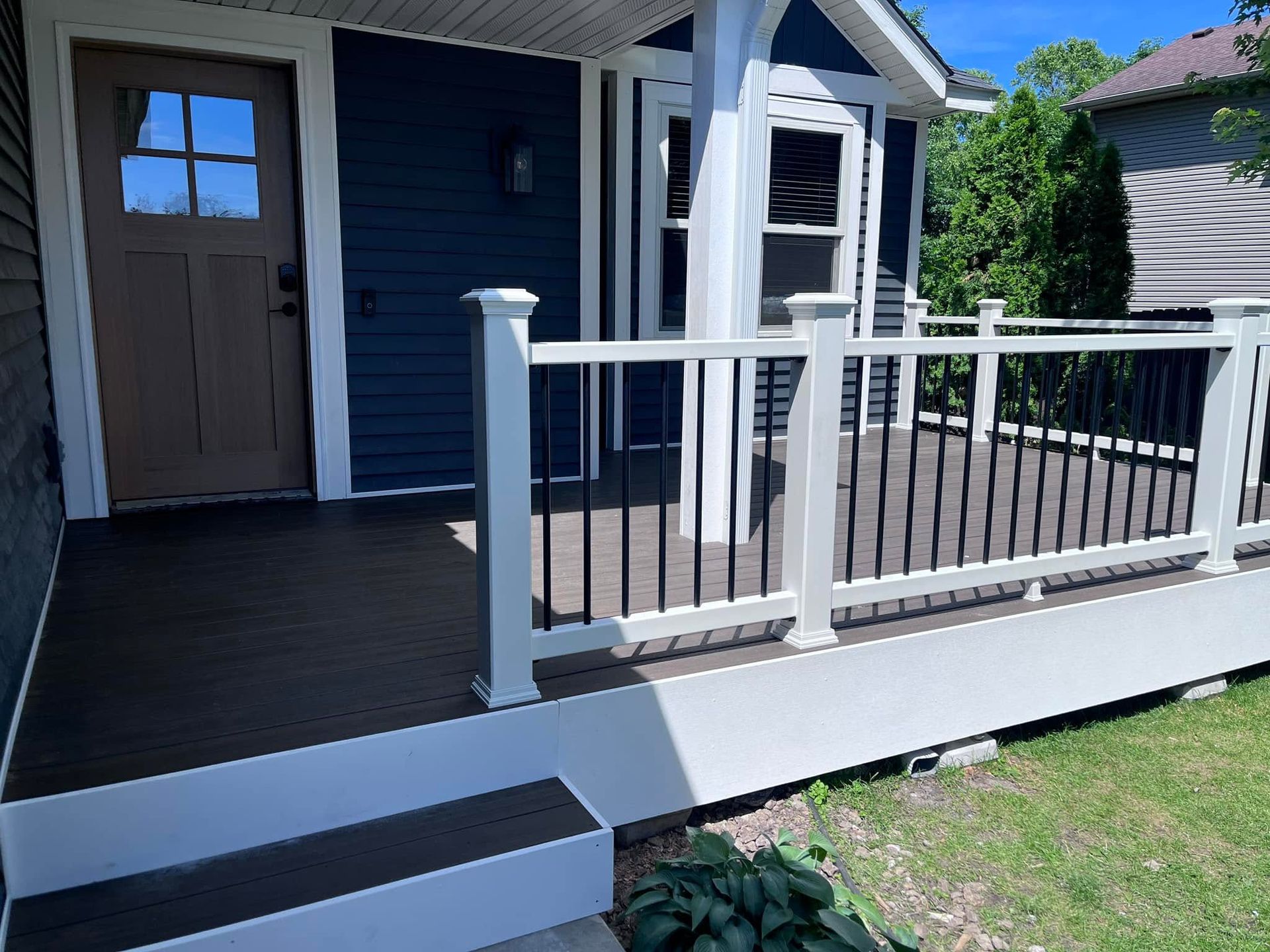Front porch with white railing, dark blue siding, and a small step up to the entrance