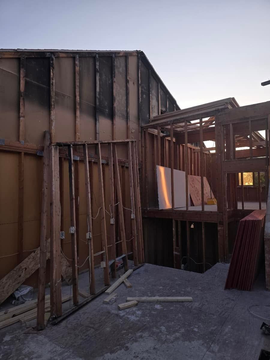 Partially framed wooden building under construction with exposed studs and gravel ground.