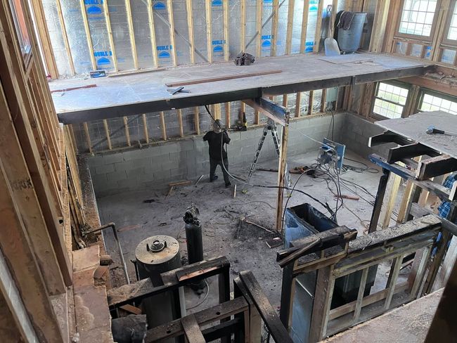 Construction site interior with exposed framing, beams, scaffolding, and a worker on the floor below