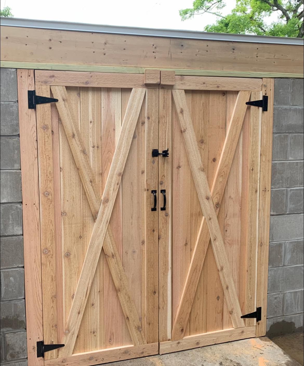 Wooden double barn doors with black hinges on a cinder block wall under a roof overhang.