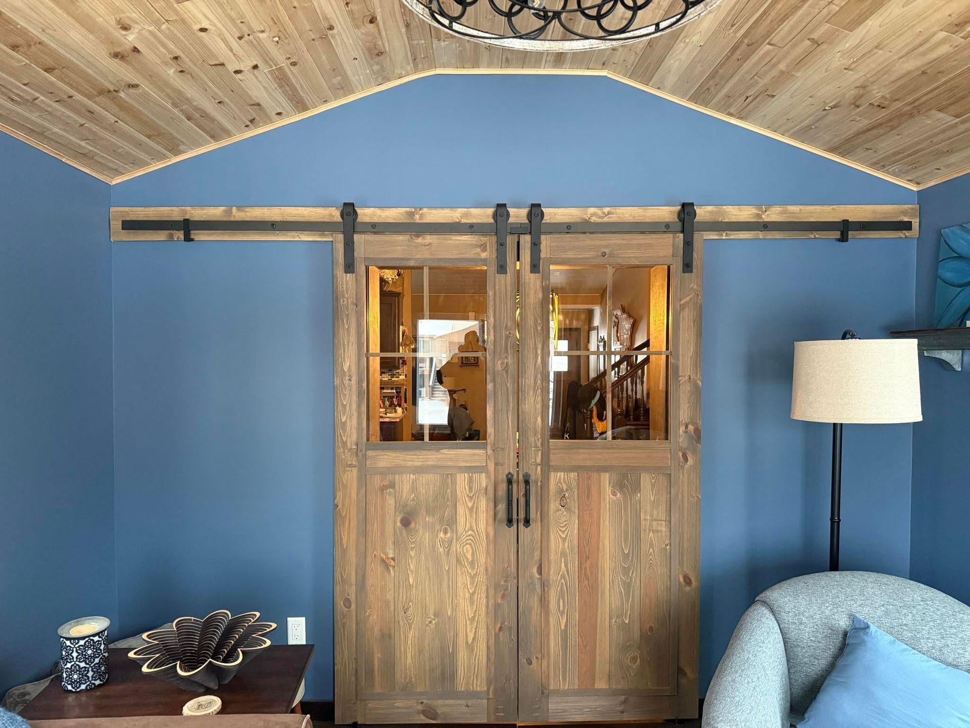 Wooden double doors with glass panes in a blue room, flanked by a floor lamp and side table