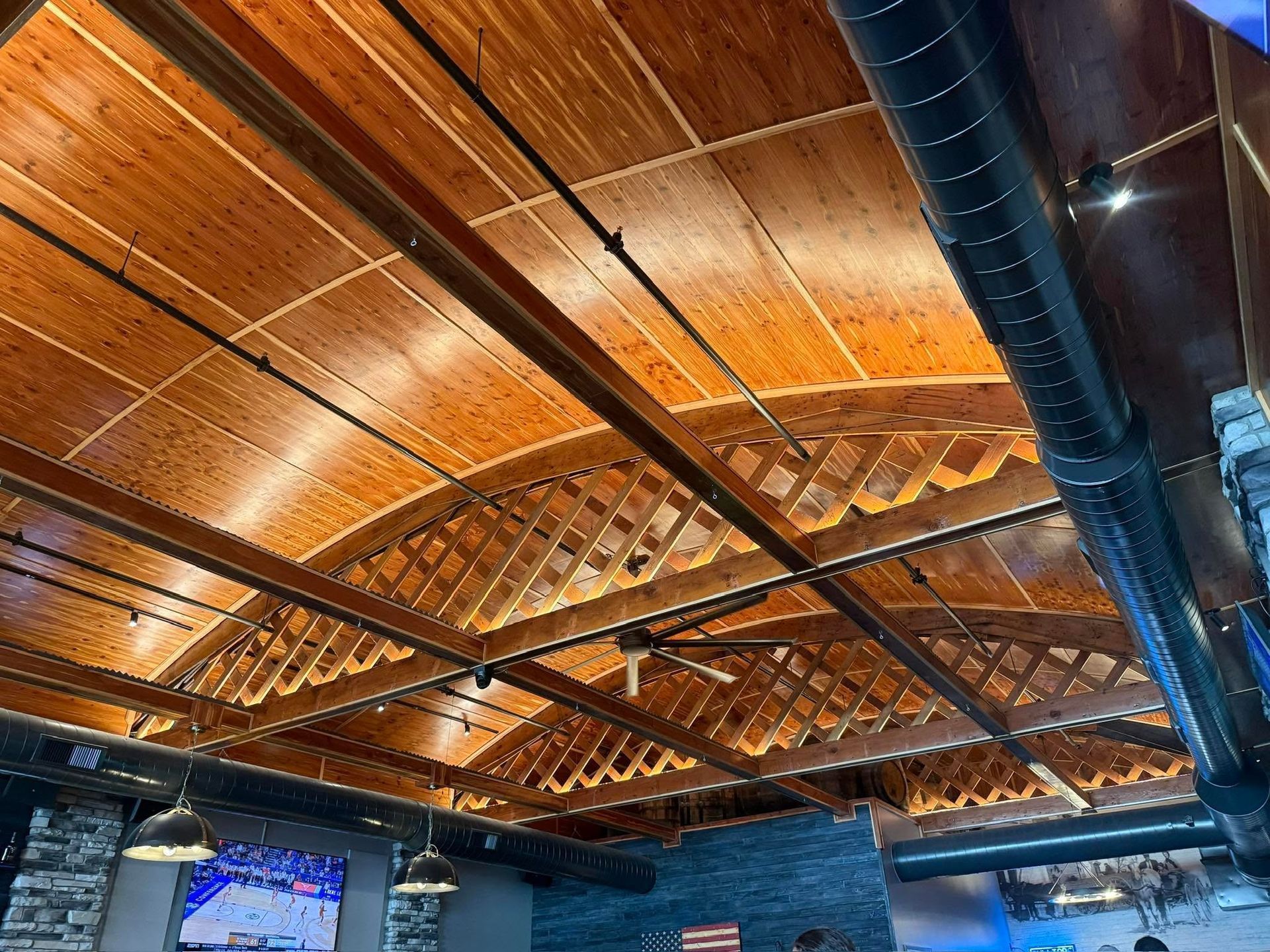 Wooden ceiling with exposed beams, blue ventilation duct, and warm ambient lighting in a room interior