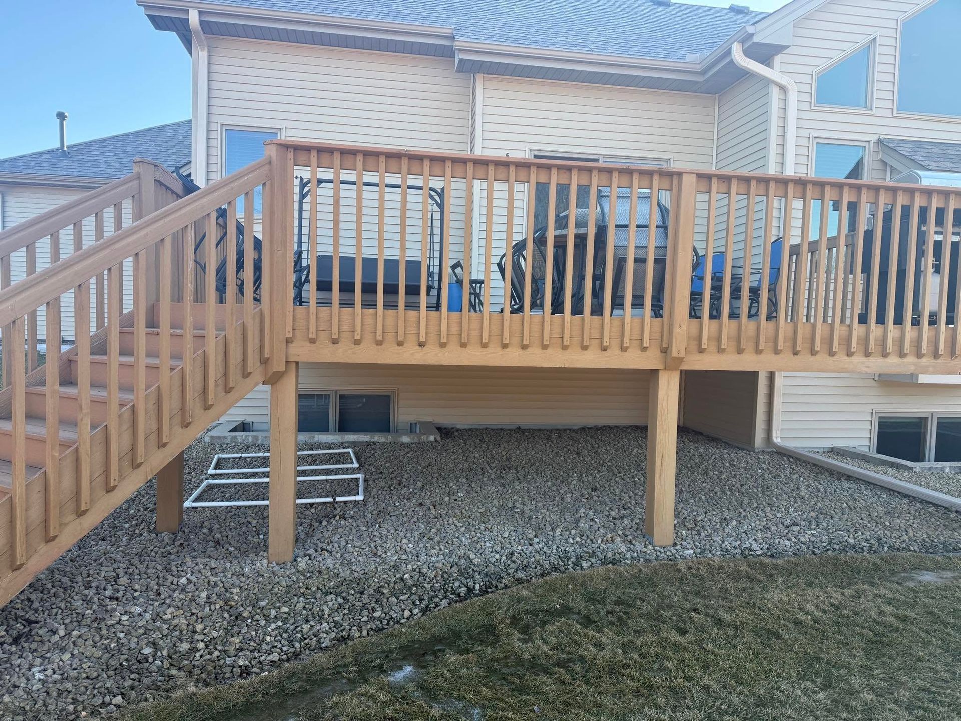 Wooden raised deck with stairs and railing attached to a house over a gravel yard.