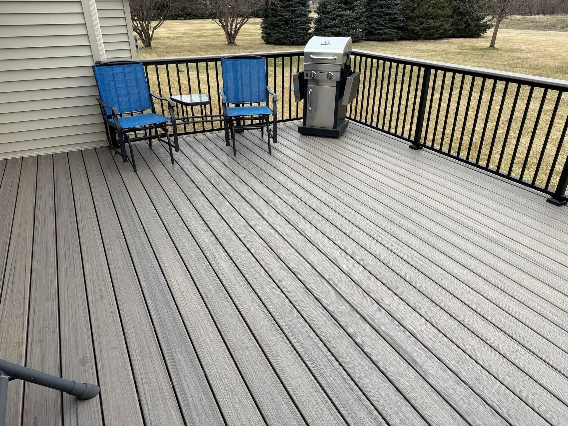 Backyard deck with two blue chairs, a grill, and a black railing overlooking a yard
