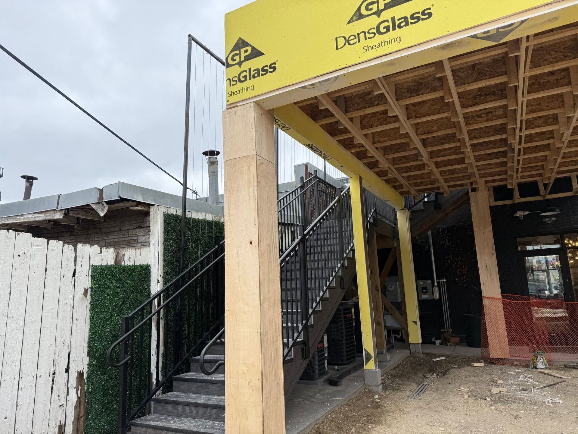 Construction site with stairway, yellow canopy, and black metal railing beside a building.