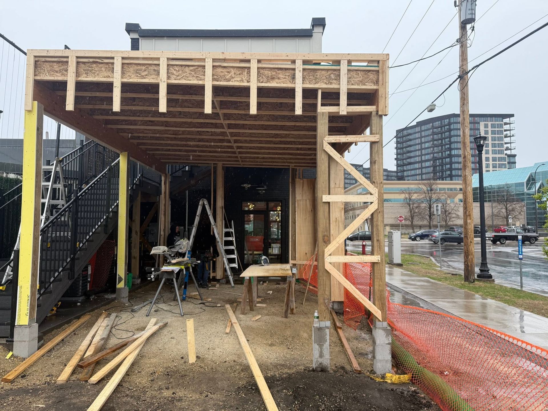 Partially built wooden carport in front of a house, with construction materials and ladders underneath