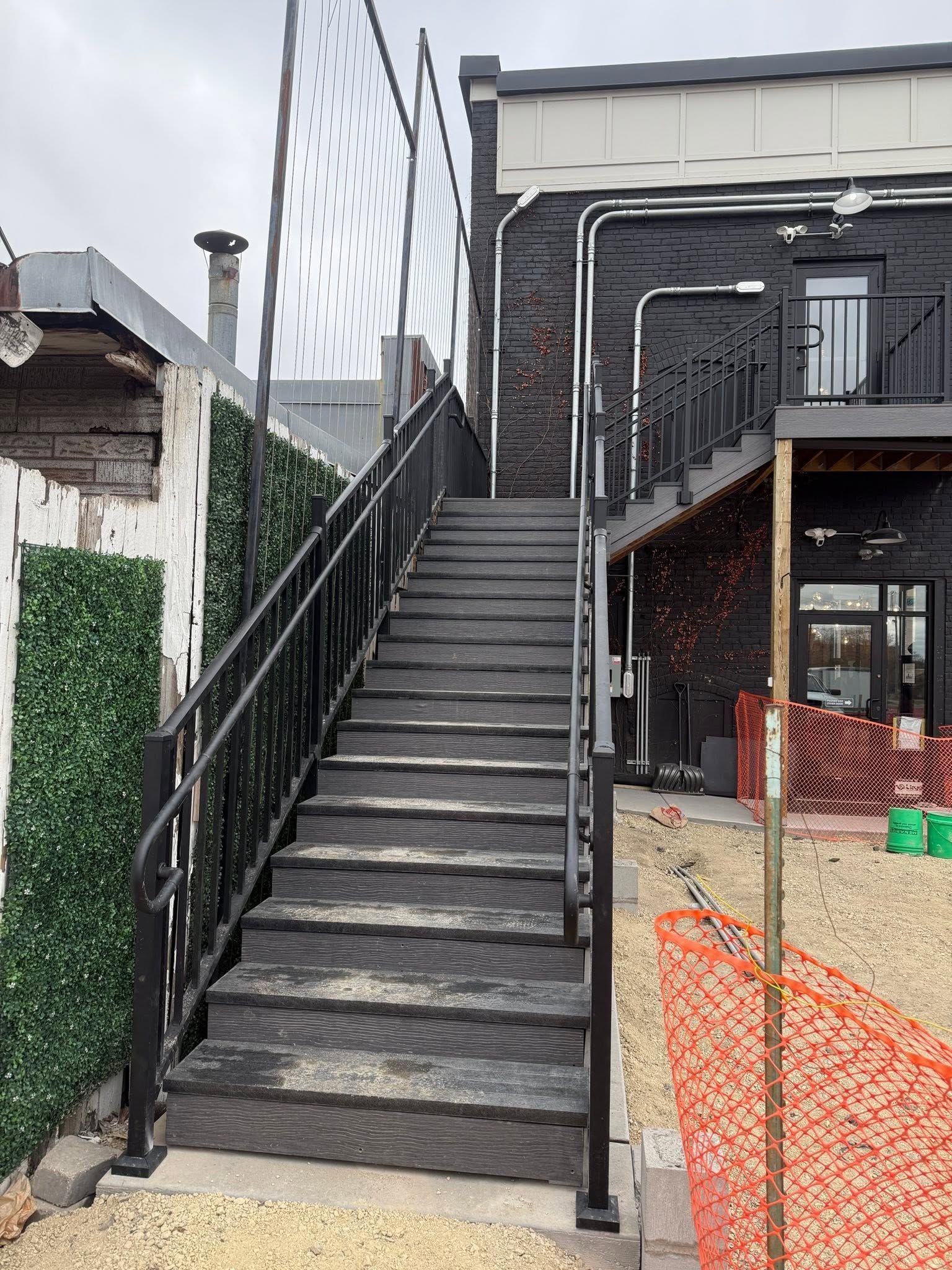 Steep outdoor black staircase beside a building, leading to an upper entrance with railings.
