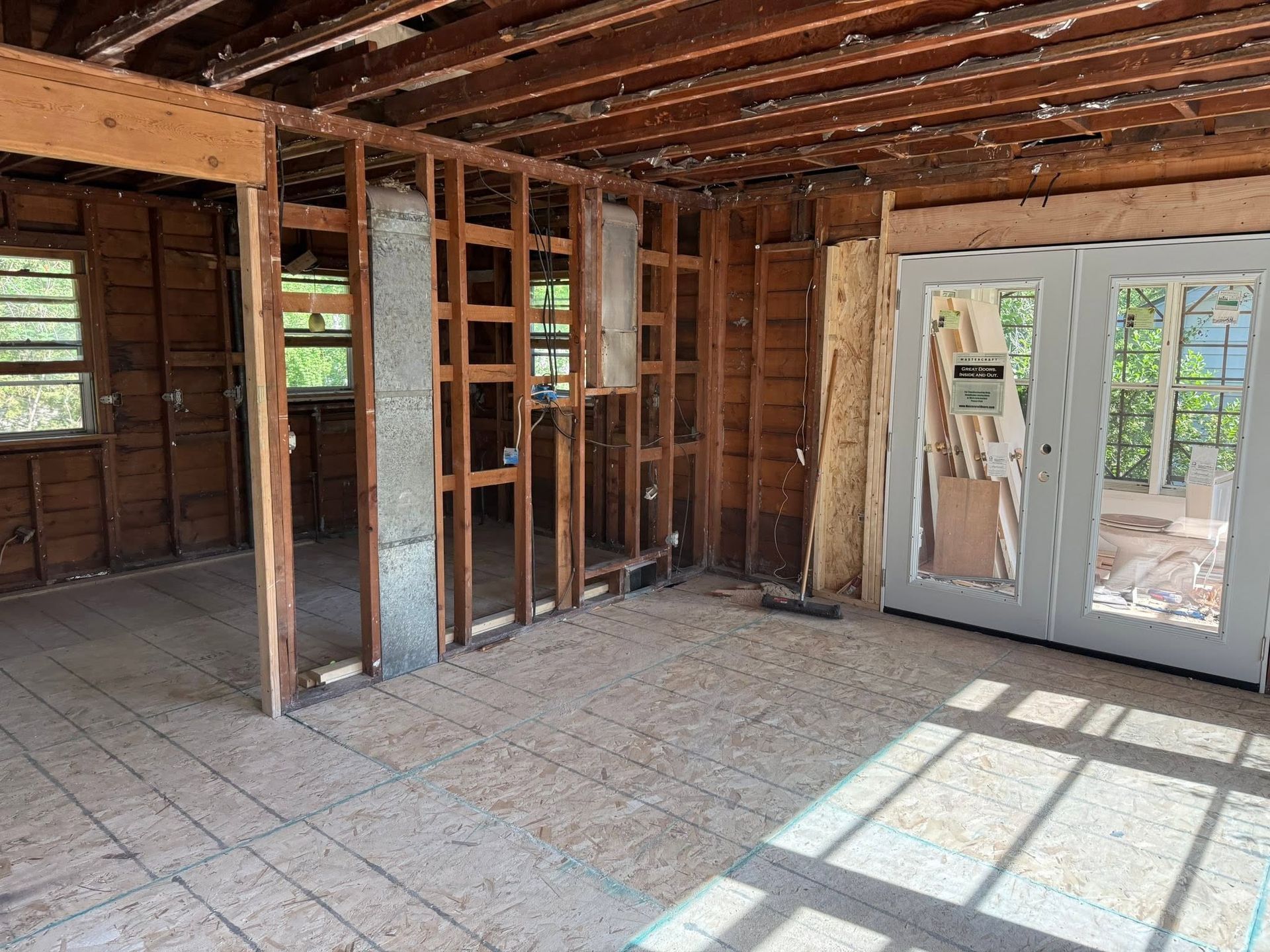 Interior of a partially demolished room with exposed studs, debris on the floor, and glass doors at right.