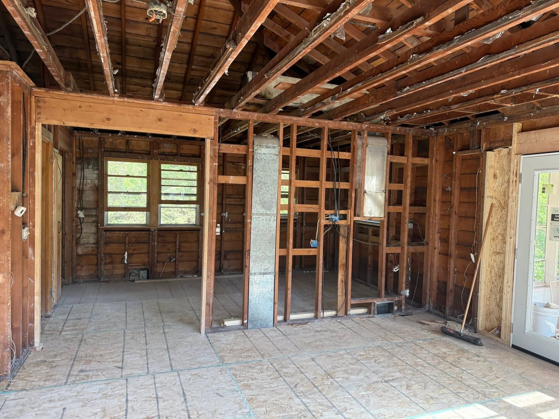 Bare room under renovation with exposed ceiling beams, open framing, and unfinished walls.