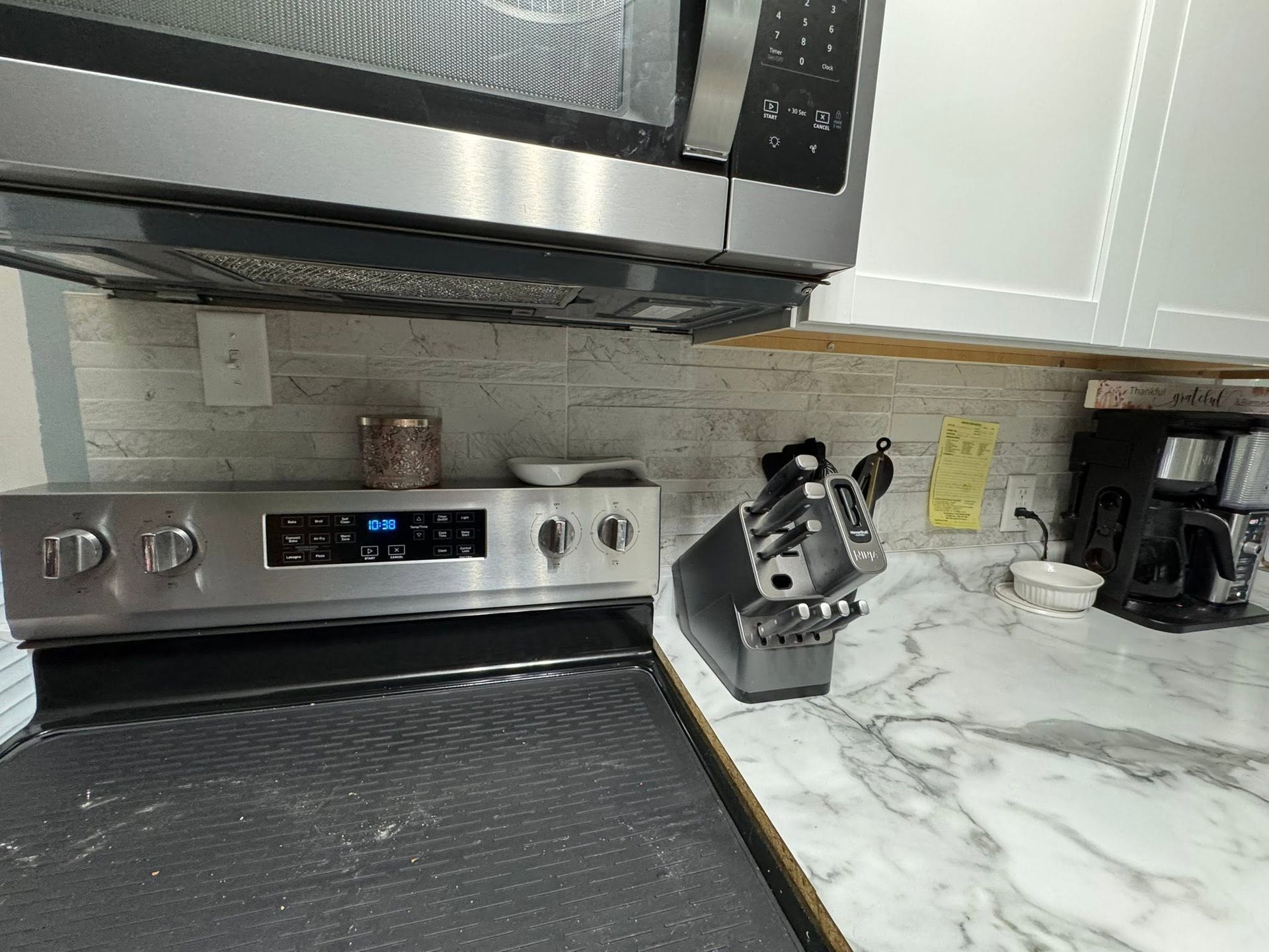 Stainless steel stove, microwave, and knife block on a white marble kitchen counter.