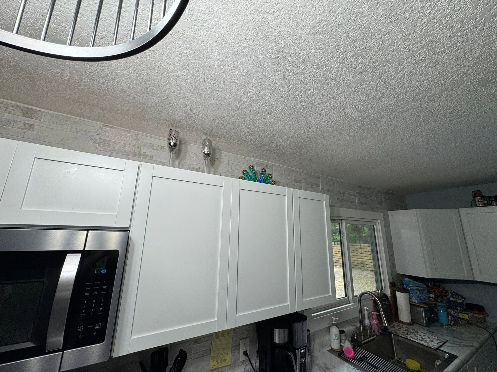 Kitchen interior with white cabinets, stainless oven, and countertop near a window with dishes.