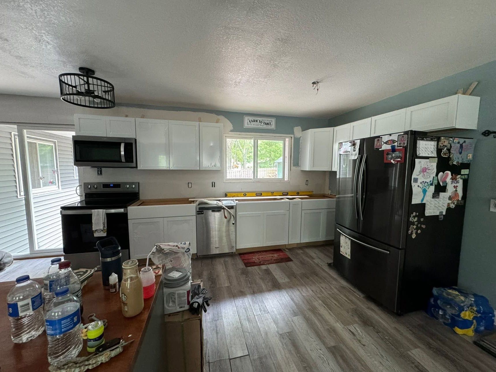 Small kitchen with white cabinets, black appliances, and a cluttered counter and table.